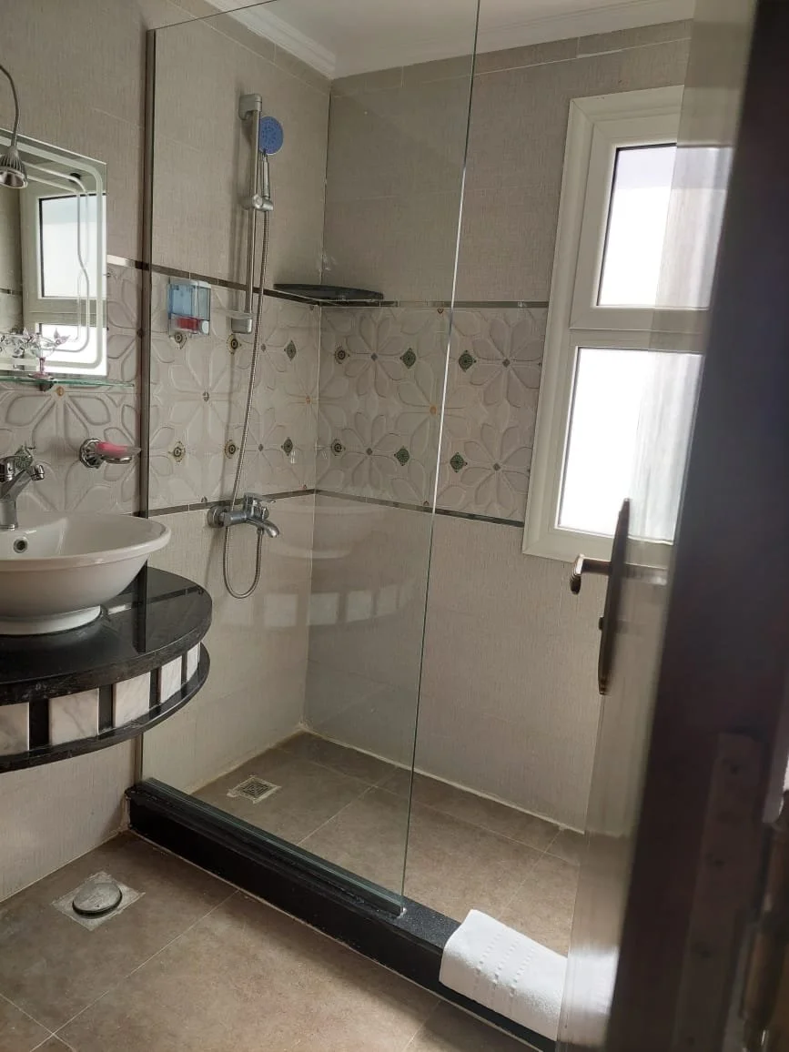 Badezimmer mit Dusche, Waschbecken, Spiegel, Fenster und Orb an der Wand.