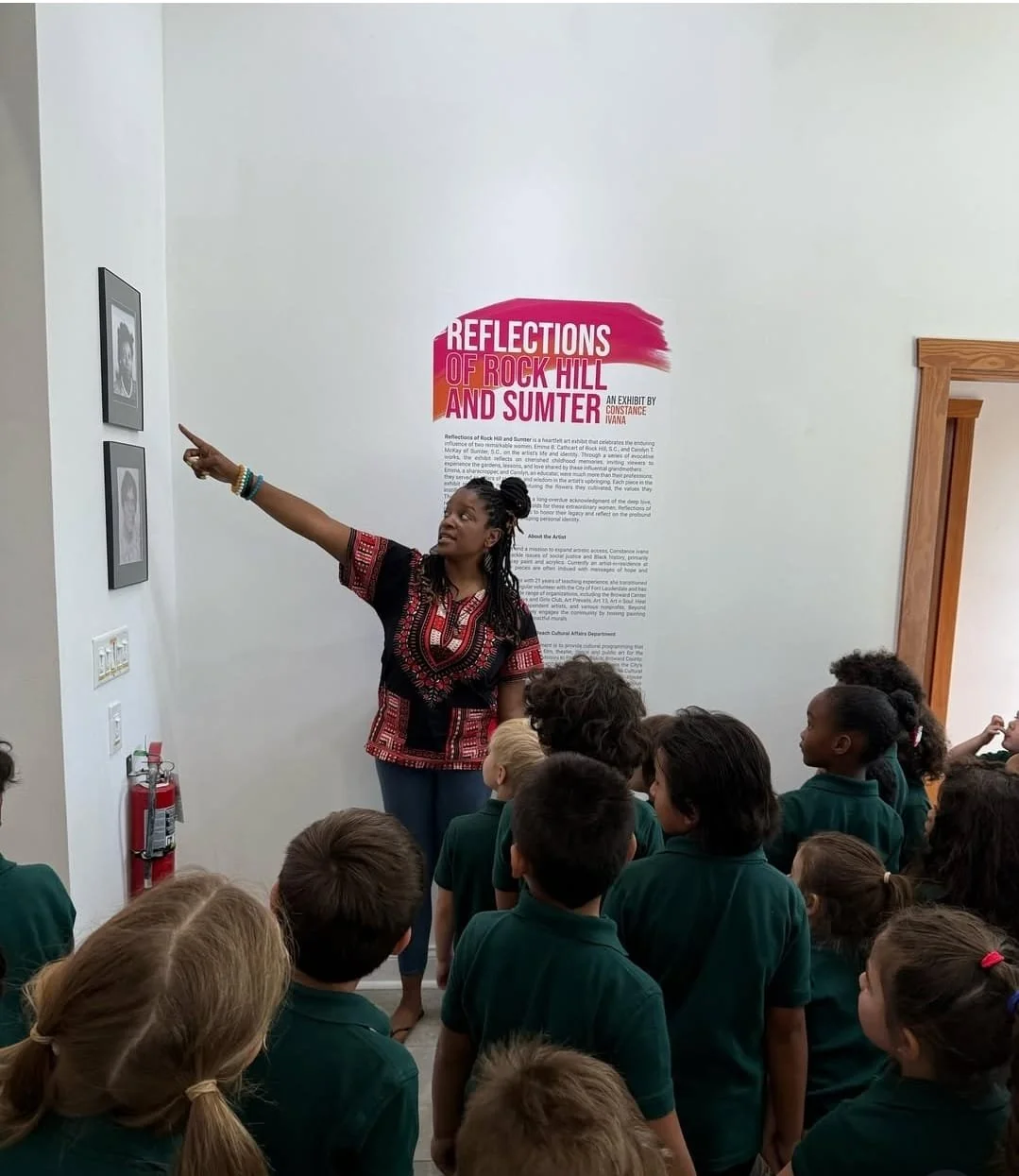 Black woman instructor leading a lesson, standing and pointing as students follow along