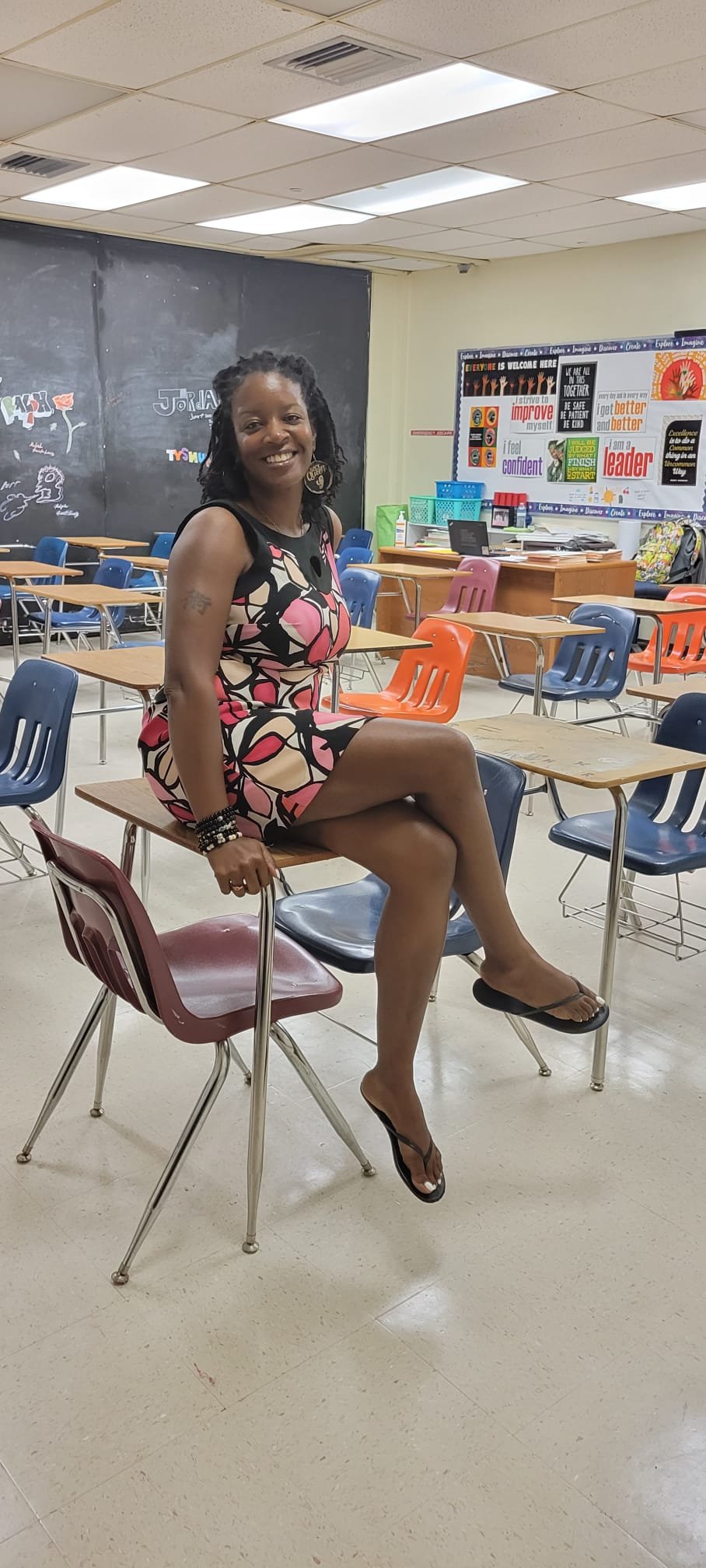 Black woman teacher smiling while seated on a desk, reflecting a positive career transition