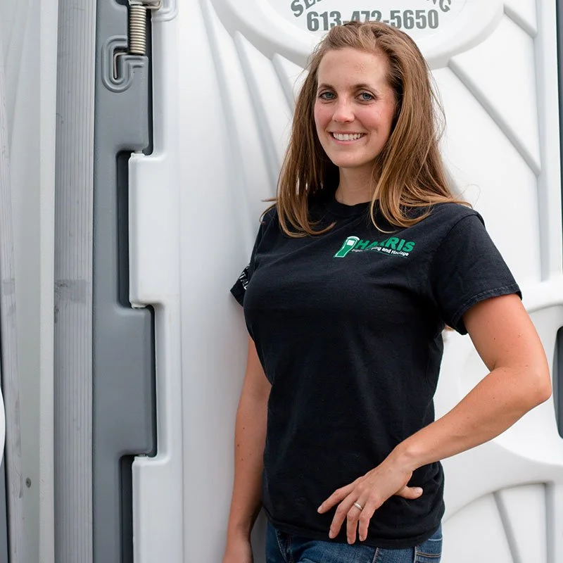 A woman with red hair wearing a black T-shirt posing beside a large white truck.