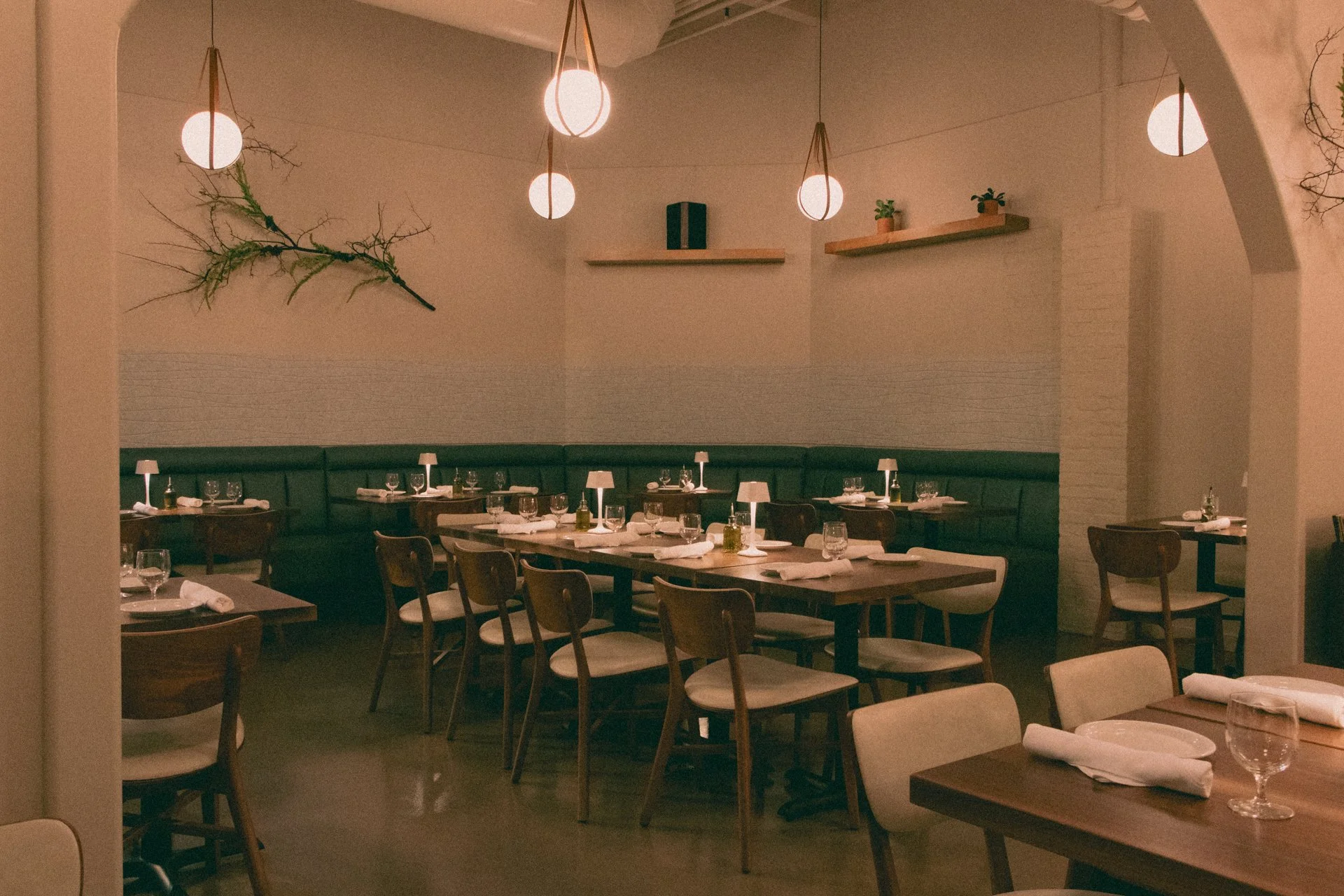 Empty restaurant with neatly arranged tables and chairs, dim lighting, hanging pendant lights, and minimal decor on walls.