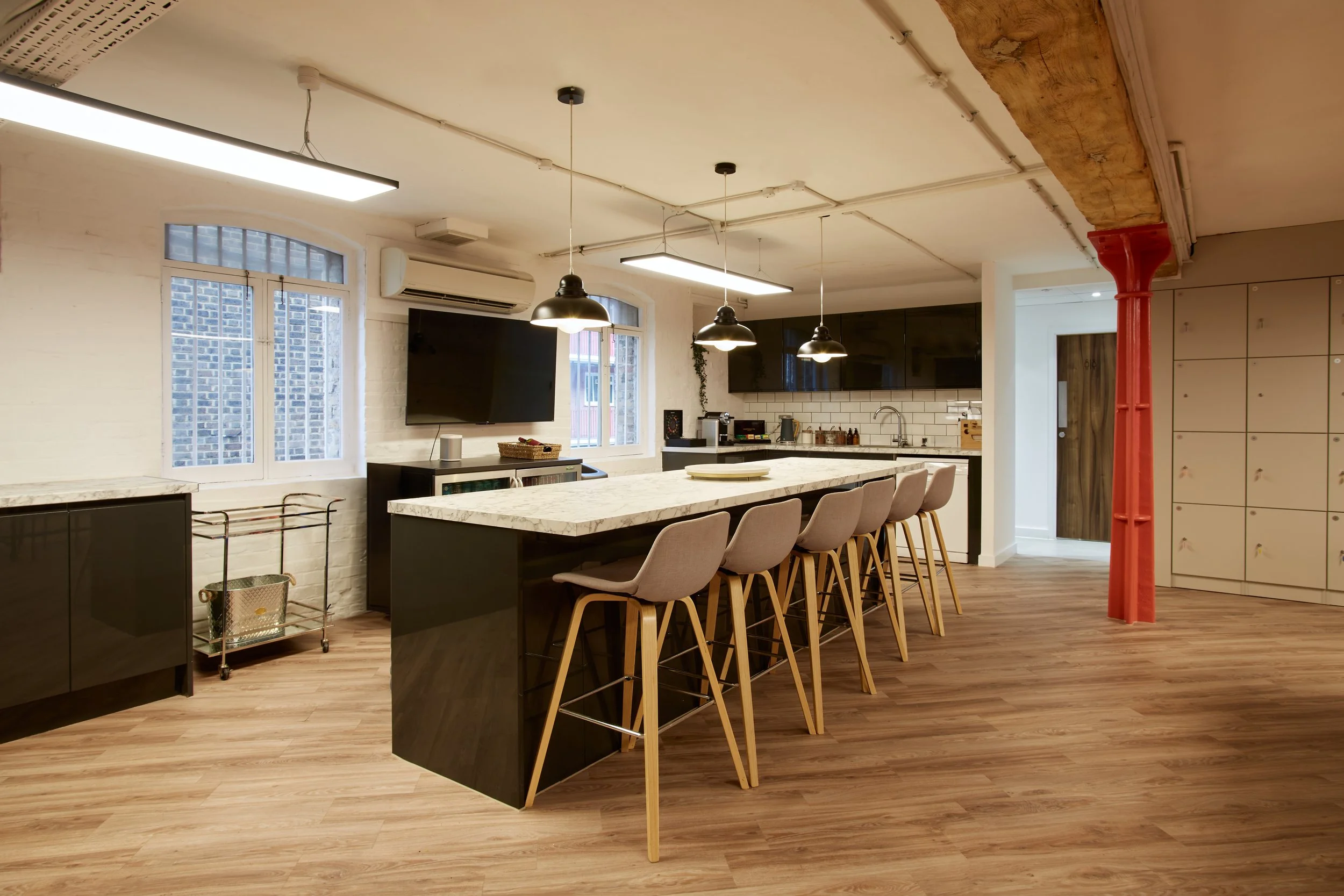 Modern kitchen with white brick walls, a large island with a marble top, beige bar stools, black cabinets, and industrial-style pendant lights.