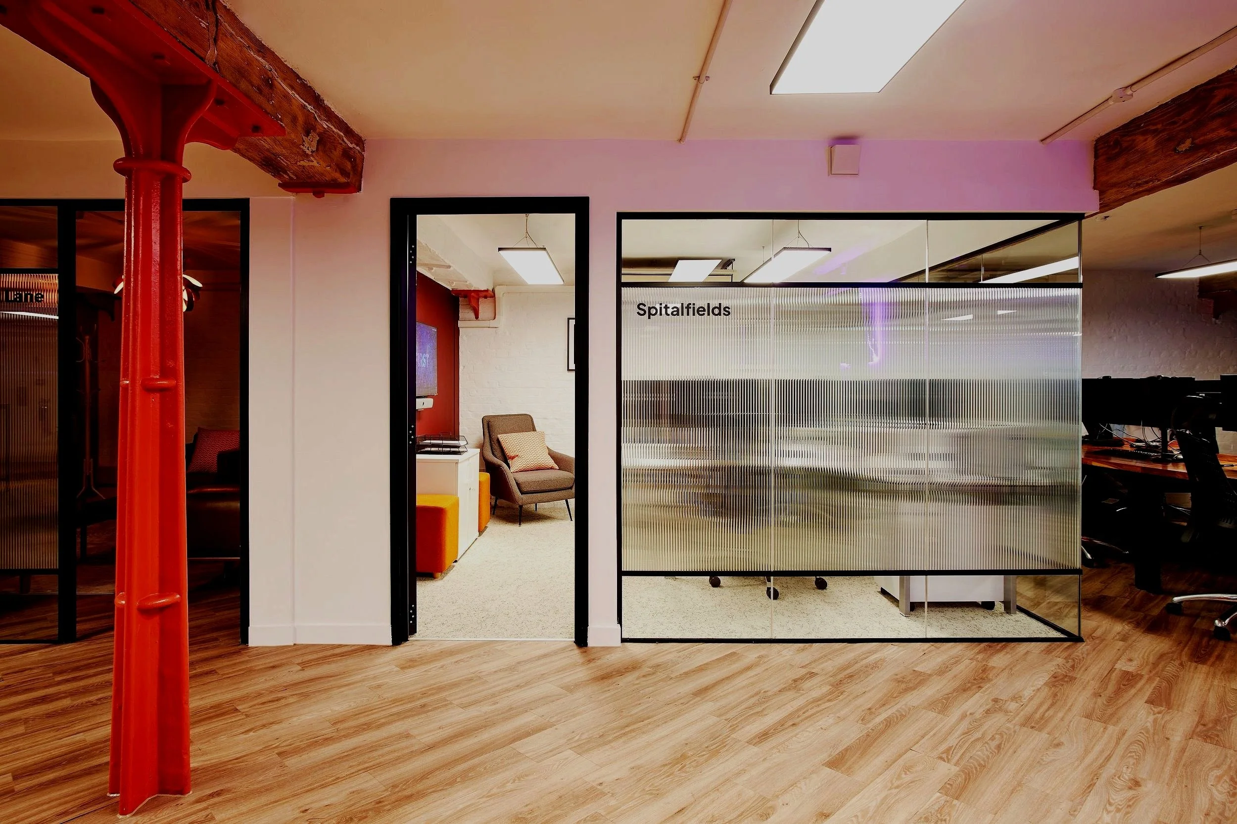 Office entrance with glass doors labeled 'Spitalfields,' visible chairs and a reception area inside, wooden beams, and wood flooring.