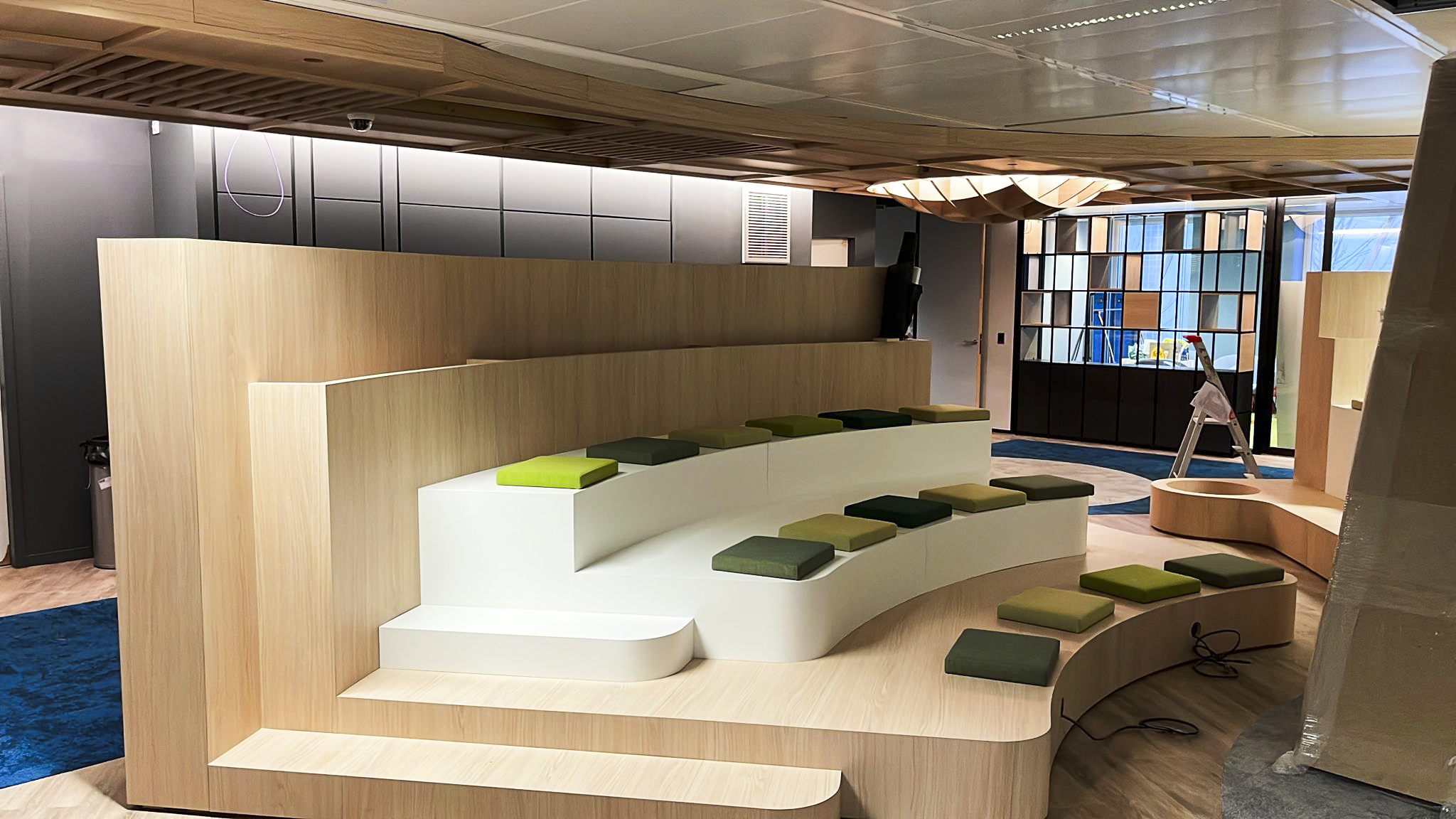Modern interior with curved wooden seating area with green and black cushions, large windows, and interior lighting.