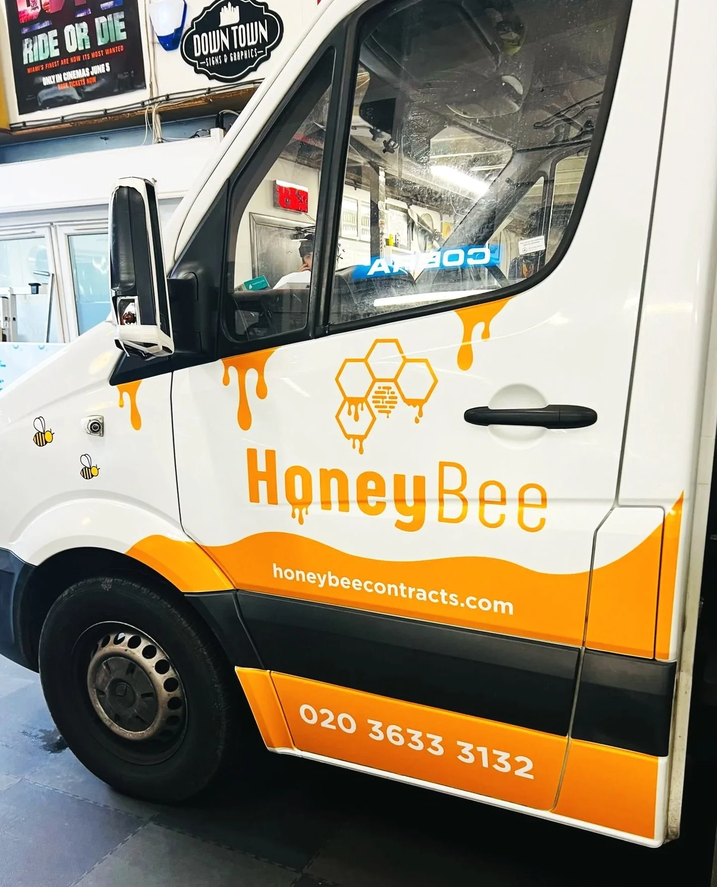 A delivery van with HoneyBee branding, orange and black colors, honey bee illustrations, honeycomb graphics, website URL honeybeecuracts.com, and phone number 020 3633 3132. The vehicle is parked indoors.
