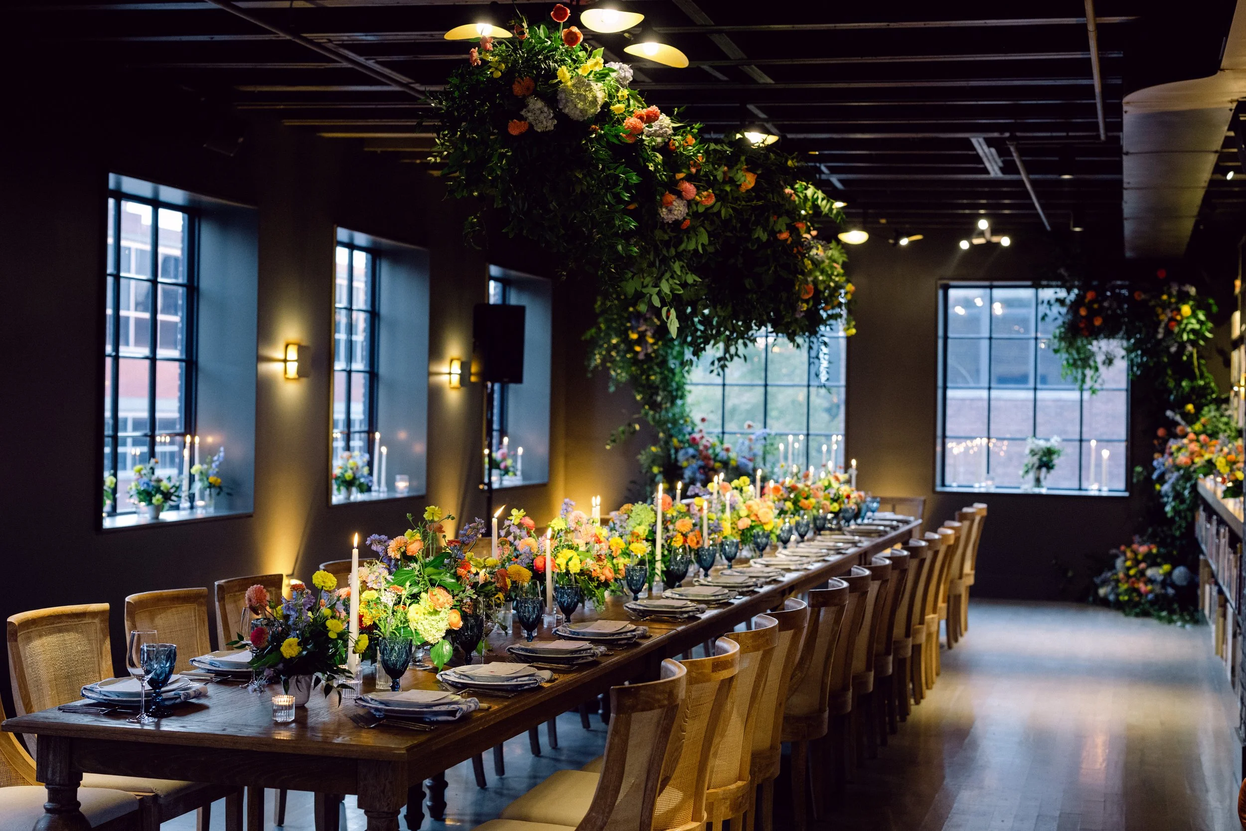 A long reception table set with a large green and colorful floral structure suspended overhead