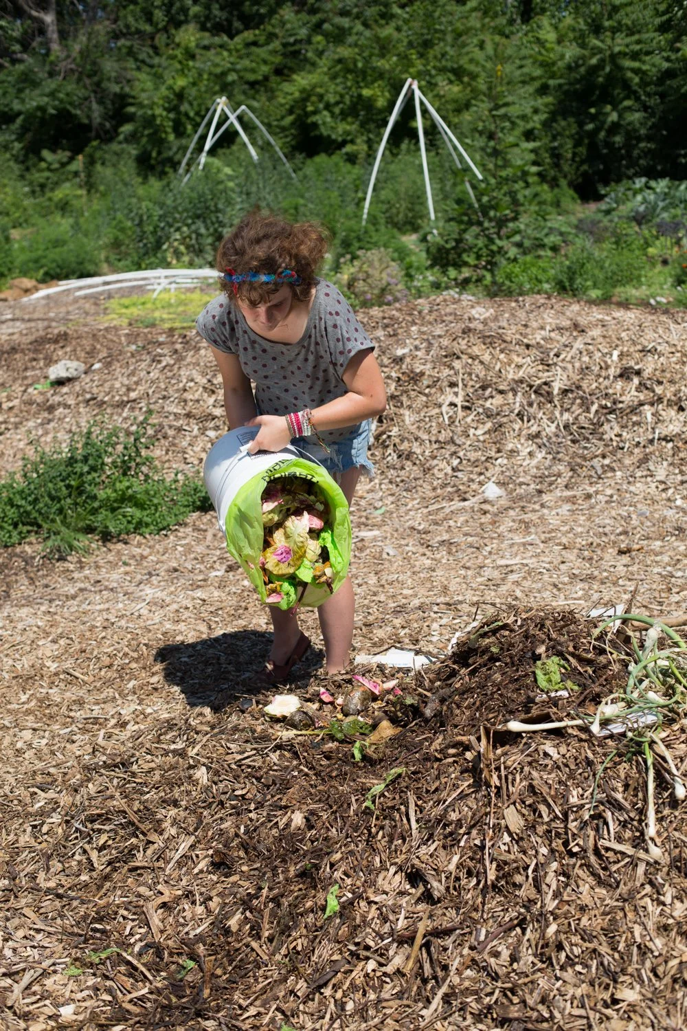 a woman dumping compost from a bin into a compost pile