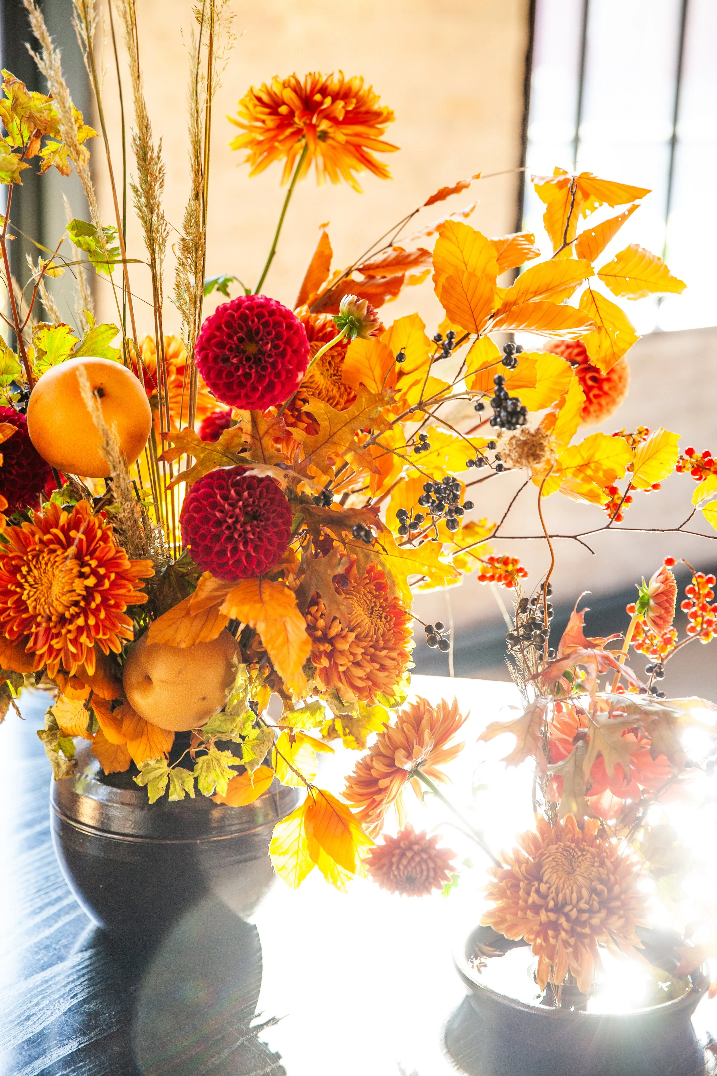 a warm floral arrangement with hues of oranges, reds with sunlilght beaming through the arrangement