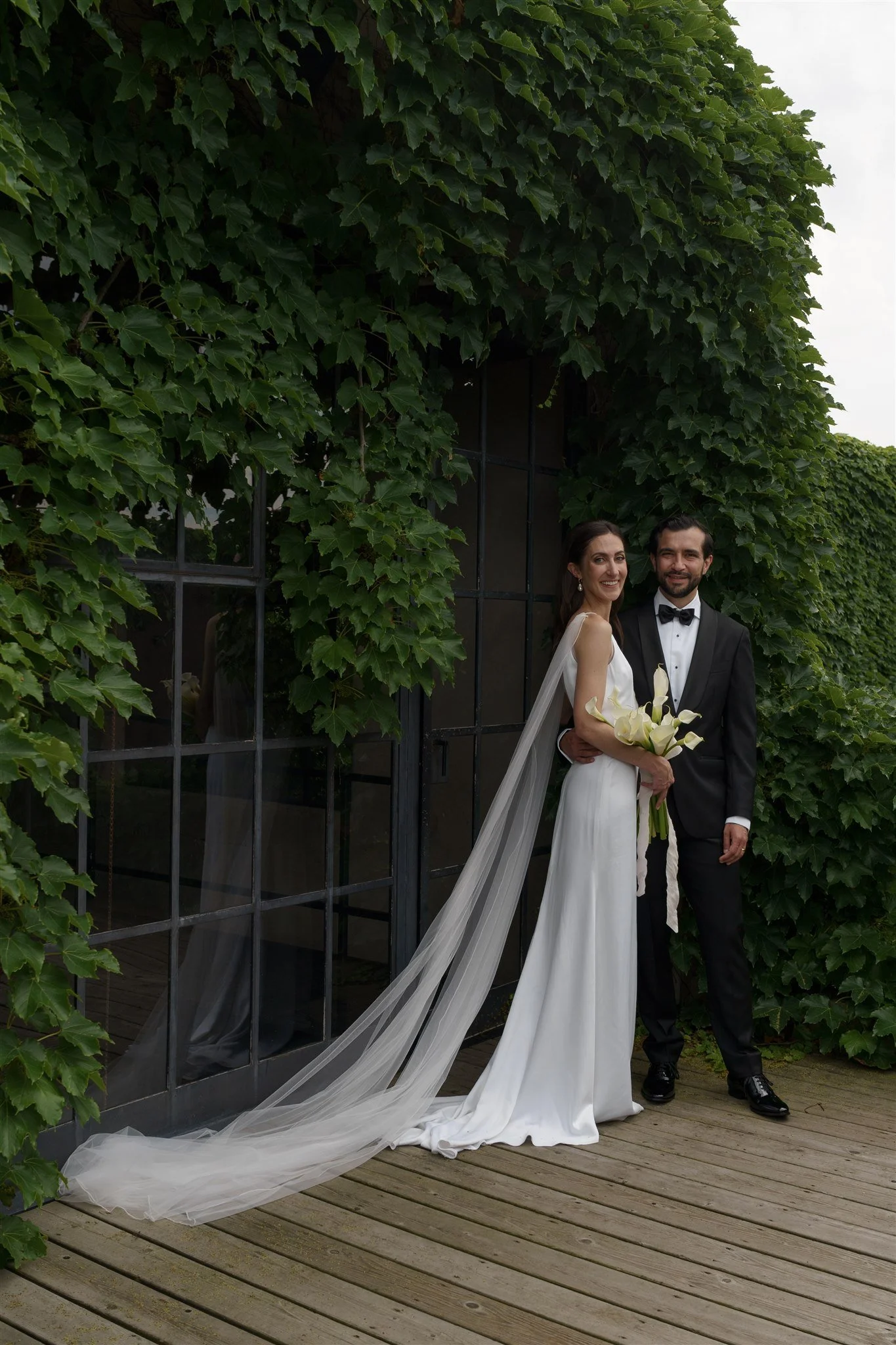 A couple poses in front of an ivy wall