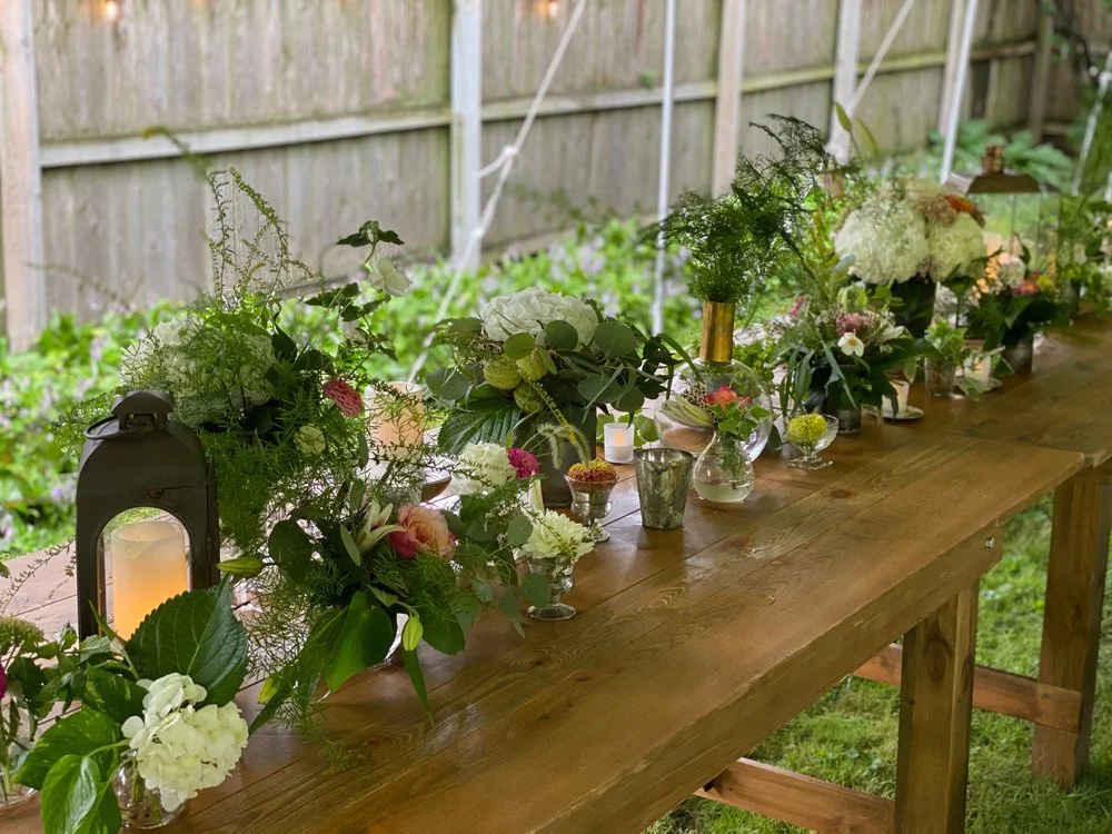 Wooden Farm table with lush organic bud vases with flowers and greenery