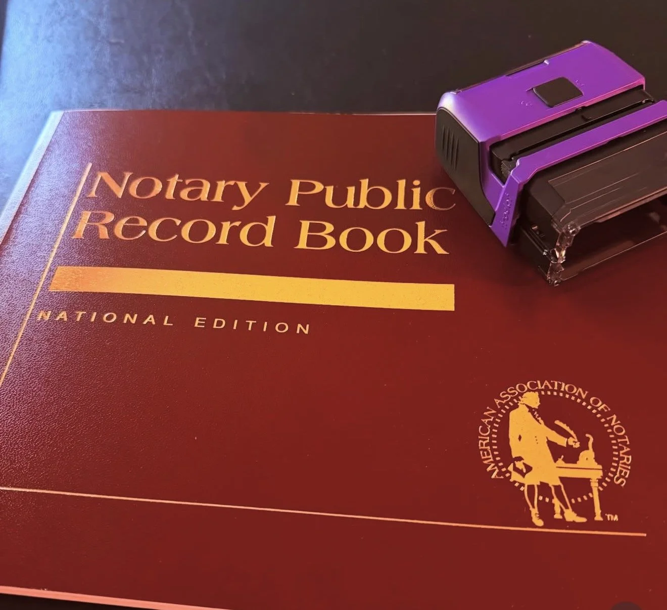 A notary public record book with a purple stamp or embossing device on top, resting on a dark surface.