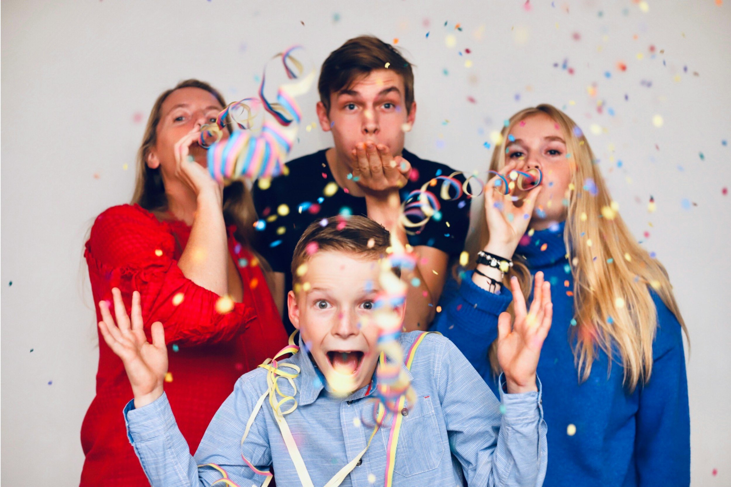 A group of people celebrating with confetti at a party, blowing party horns, with excited expressions.