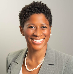 Professional woman smiling, wearing a light gray blazer, pearl necklace, and pearl earrings.