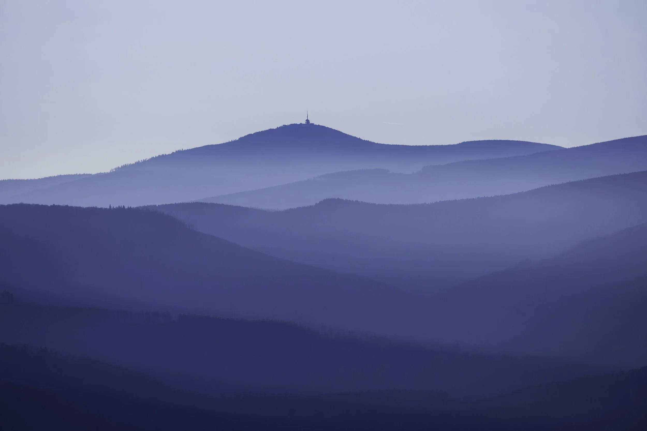 Layers of blue mountain ranges fading into the distance with a communication tower on top of the highest peak.