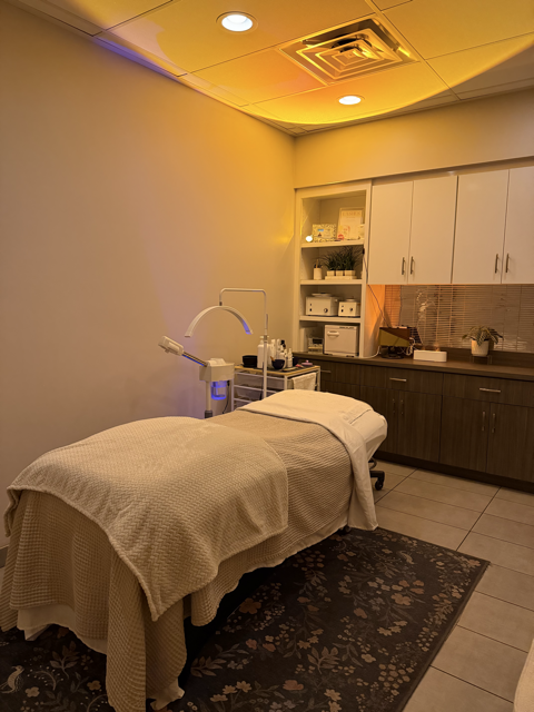 Medical examination room with a massage table, medical equipment, and cabinets, lit by warm colored lighting.