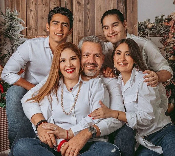 A family of six posing together in front of Christmas decorations, smiling warmly.