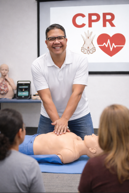 An instructor demonstrates CPR on a training mannequin during a CPR class, with a presentation slide showing a heart and hands practicing chest compressions in the background.