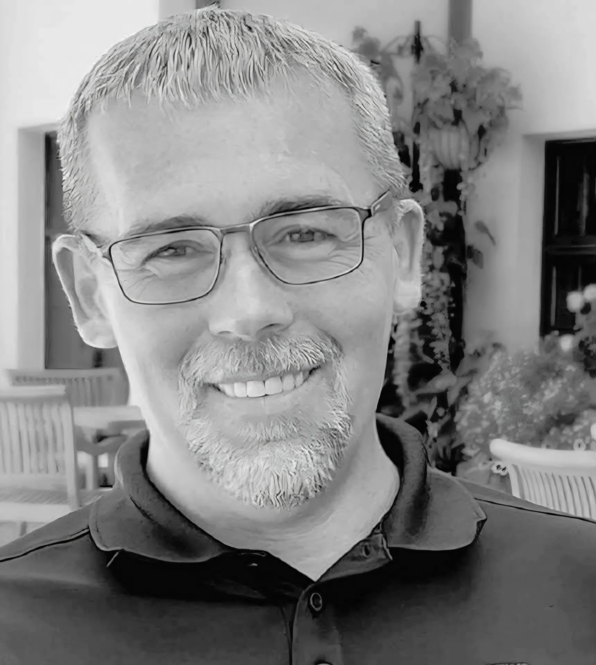 Black and white photo of middle-aged man with glasses, a goatee, and short hair, smiling indoors.