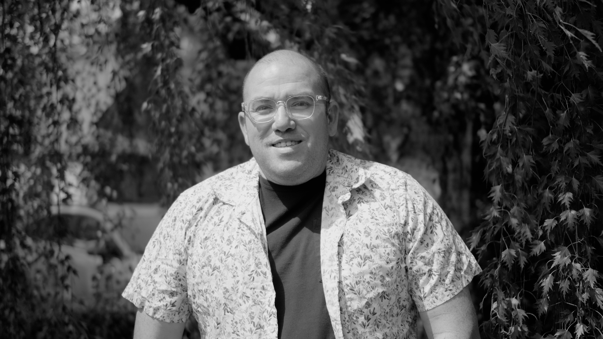 A man posing in front of a willow tree with a white color shirt in a black and white photo.