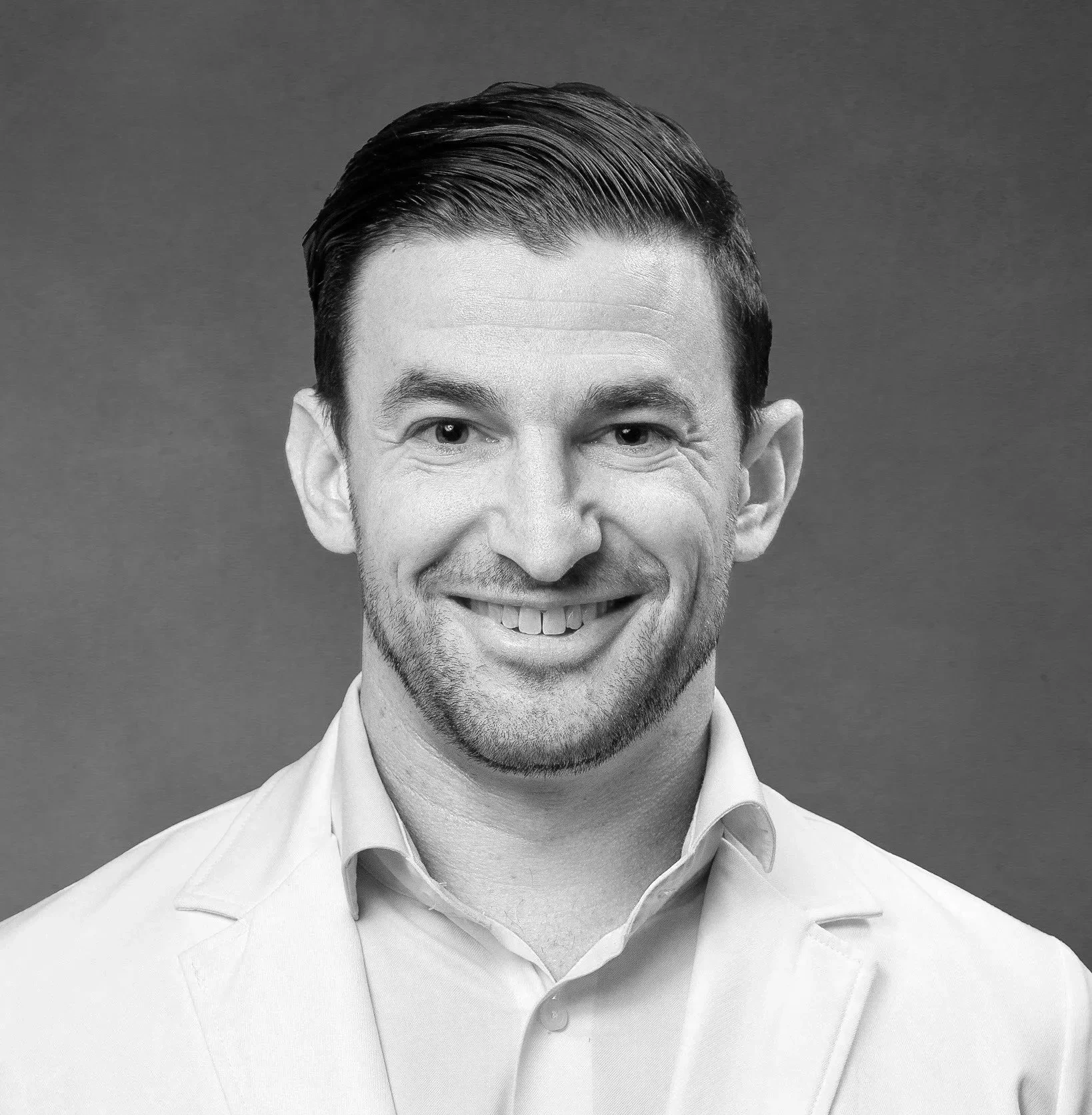 Black and white portrait of a smiling man in a collared shirt, against a plain background.