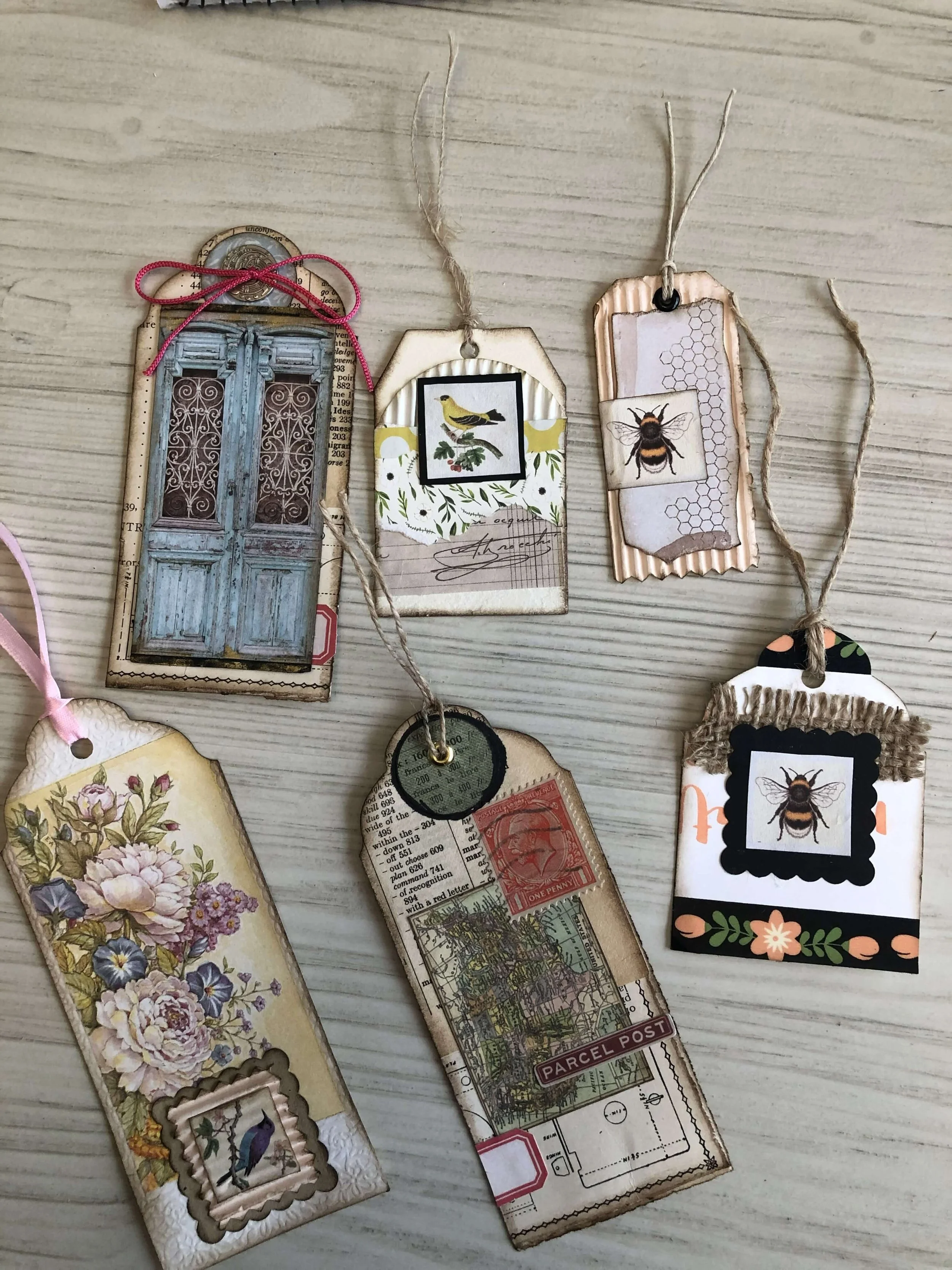 Collection of decorative tags and labels with various designs, including floral, bird, bee, door, and map motifs, tied with string.