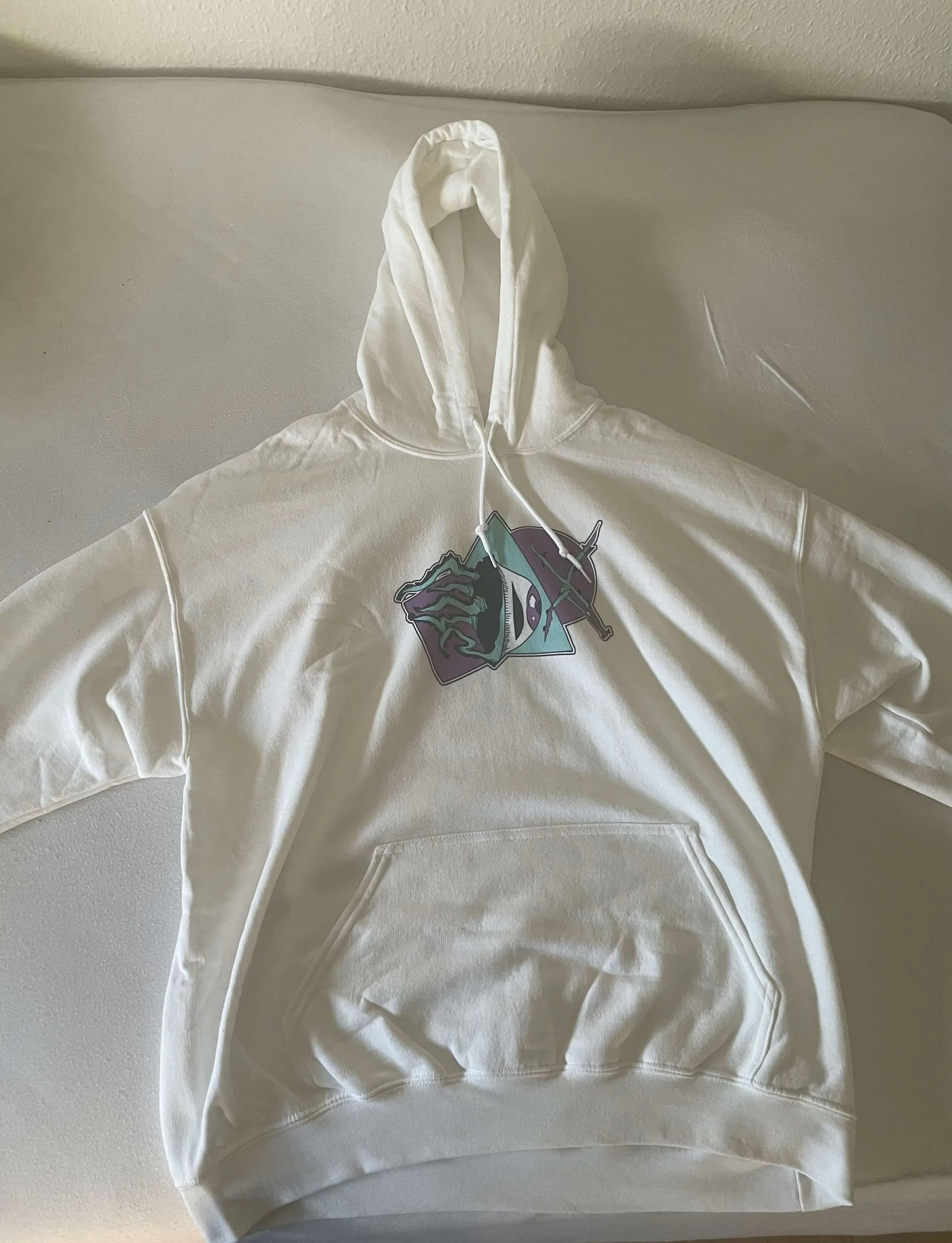 A white hoodie with colorful graphic on the front laid flat on a white surface.