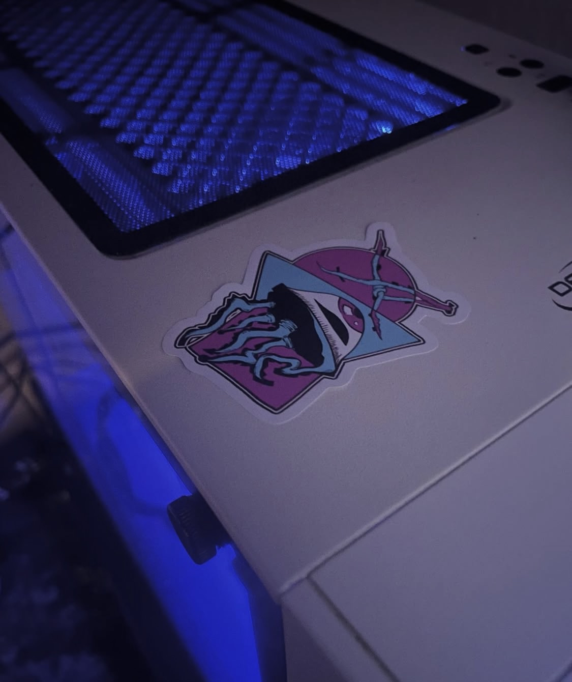 A sticker featuring a stylized illustration of a lion's head with a mountain range in the background, and a sword crossing behind a triangle, with a pink and blue color scheme, on a laptop with a blue-lit keyboard.