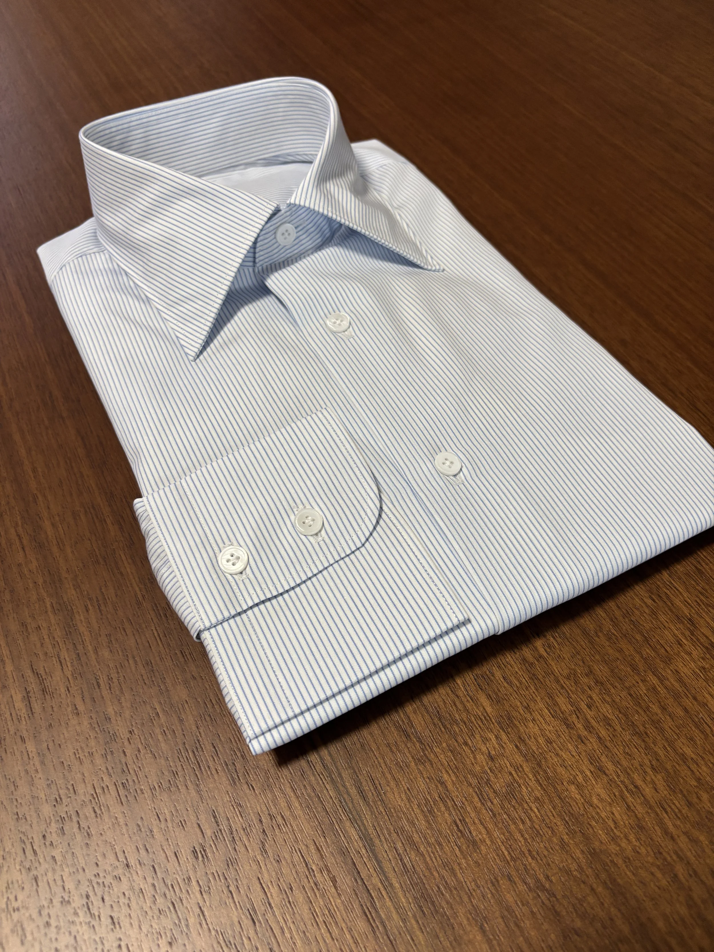 Custom made blue and white pencil stripe dress shirt with mother of pearl shell buttons on a walnut wooden table.