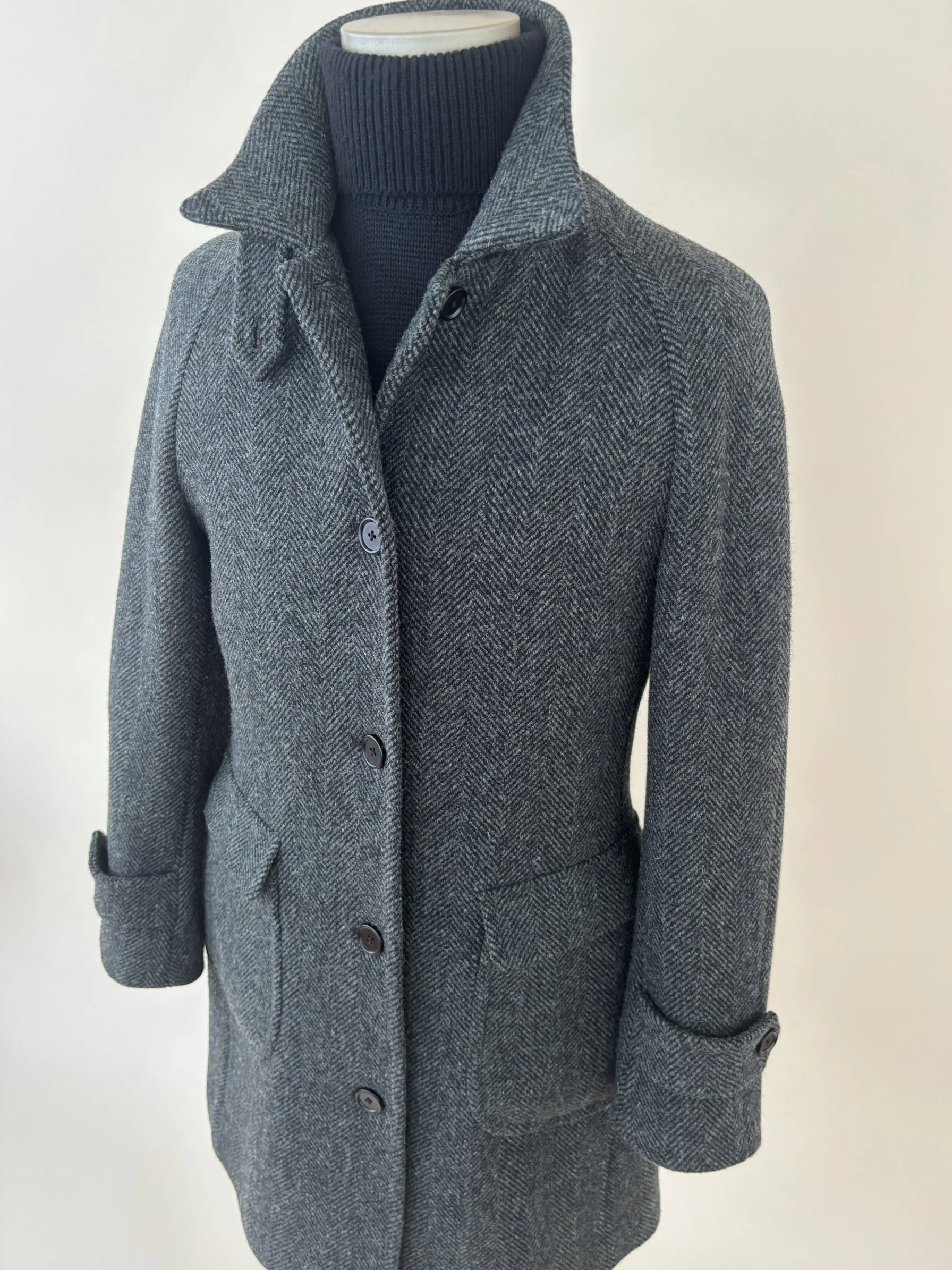 Custom made green and black tweed overcoat with raglan sleeve and black wool turtleneck on a form against a tan backdrop.