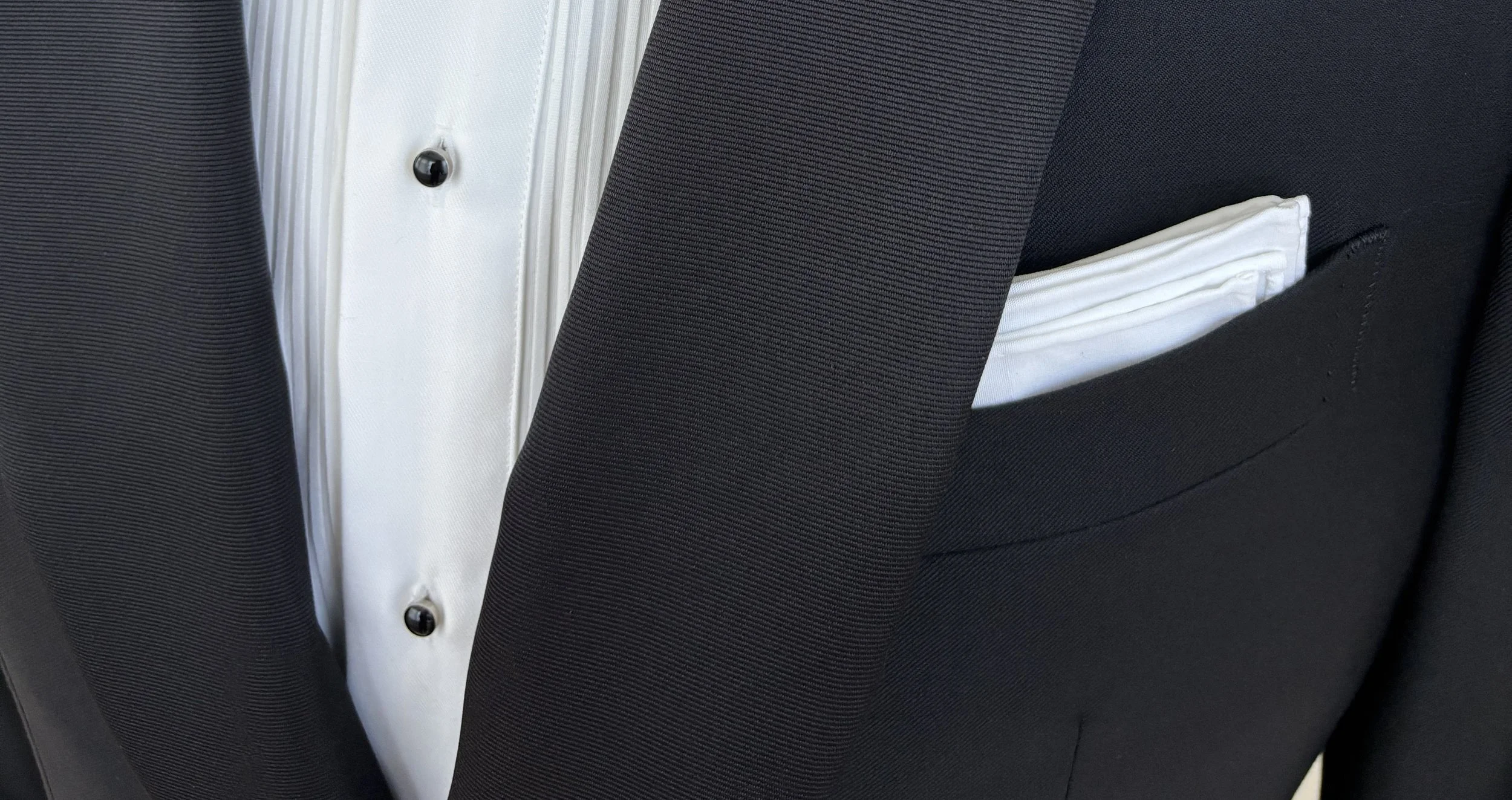 Close-up of a black suit jacket featuring a crisp white pocket square.