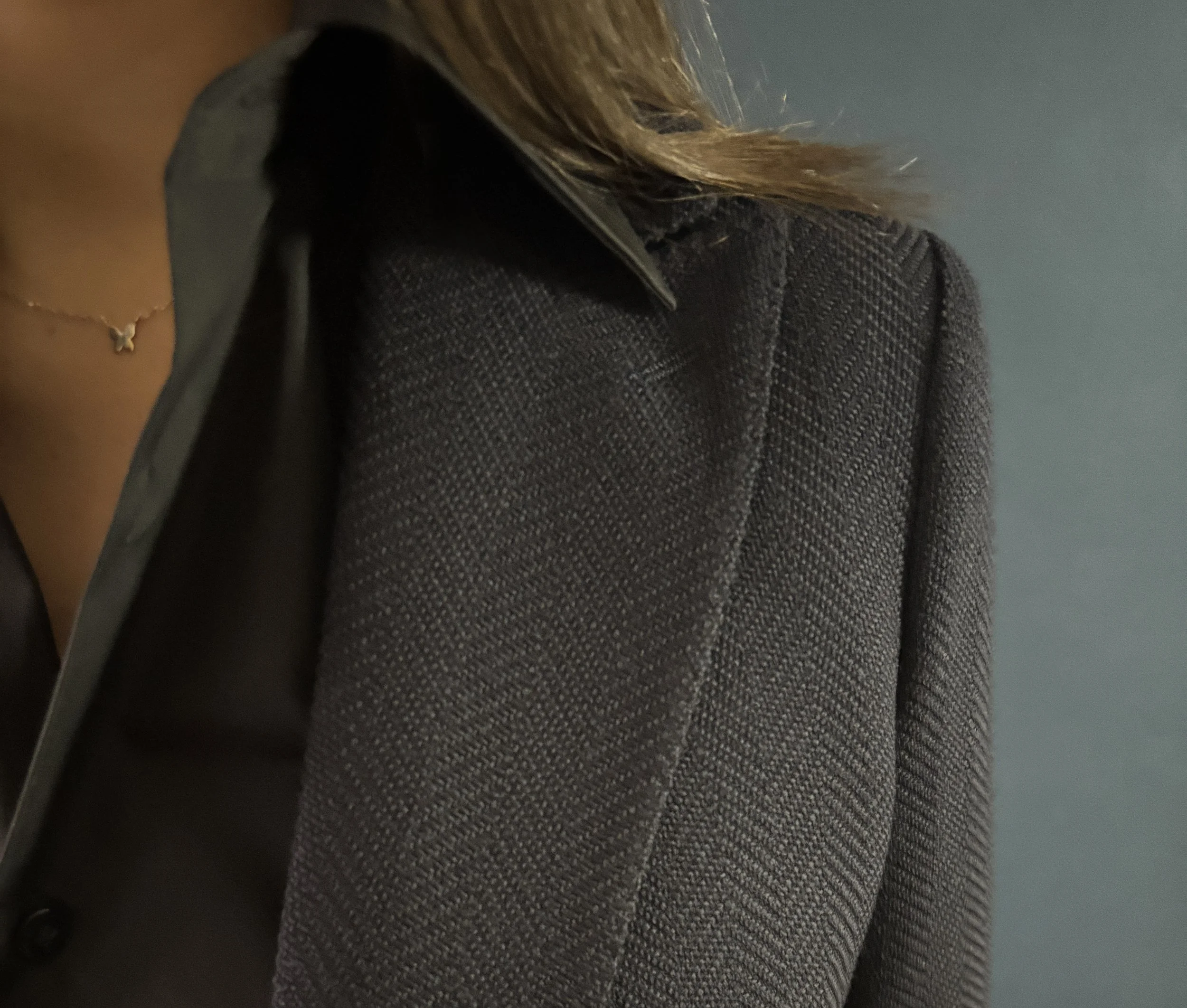 A close up of a custom made women's suit peak lapel in navy herringbone Stylbiella fabric with a custom made women's dress shirt against and indigo blue backdrop.