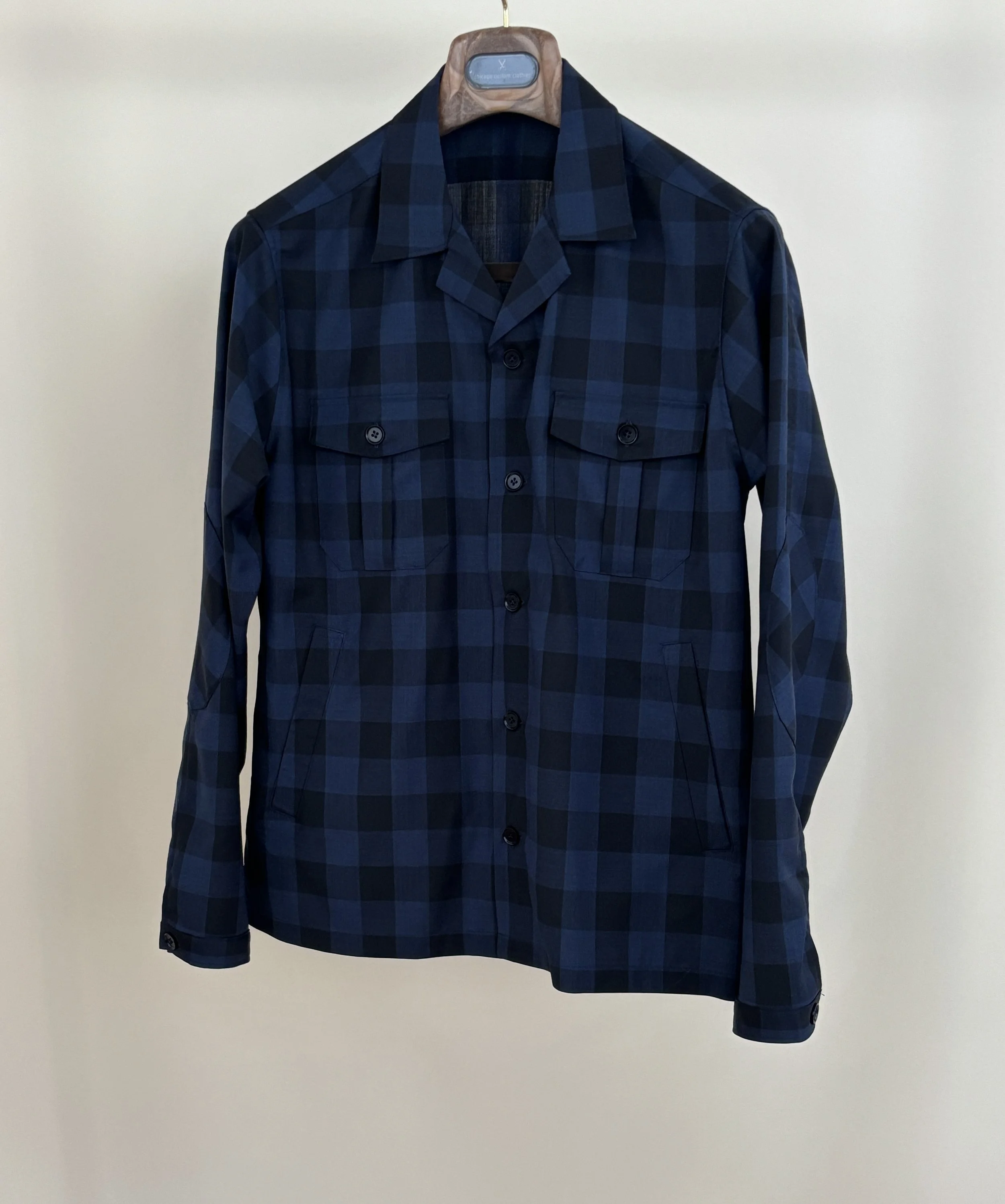 A custom made navy and black checked overskirt in a Reda merino wool fabric on a wooden hanger in front of a tan backdrop.