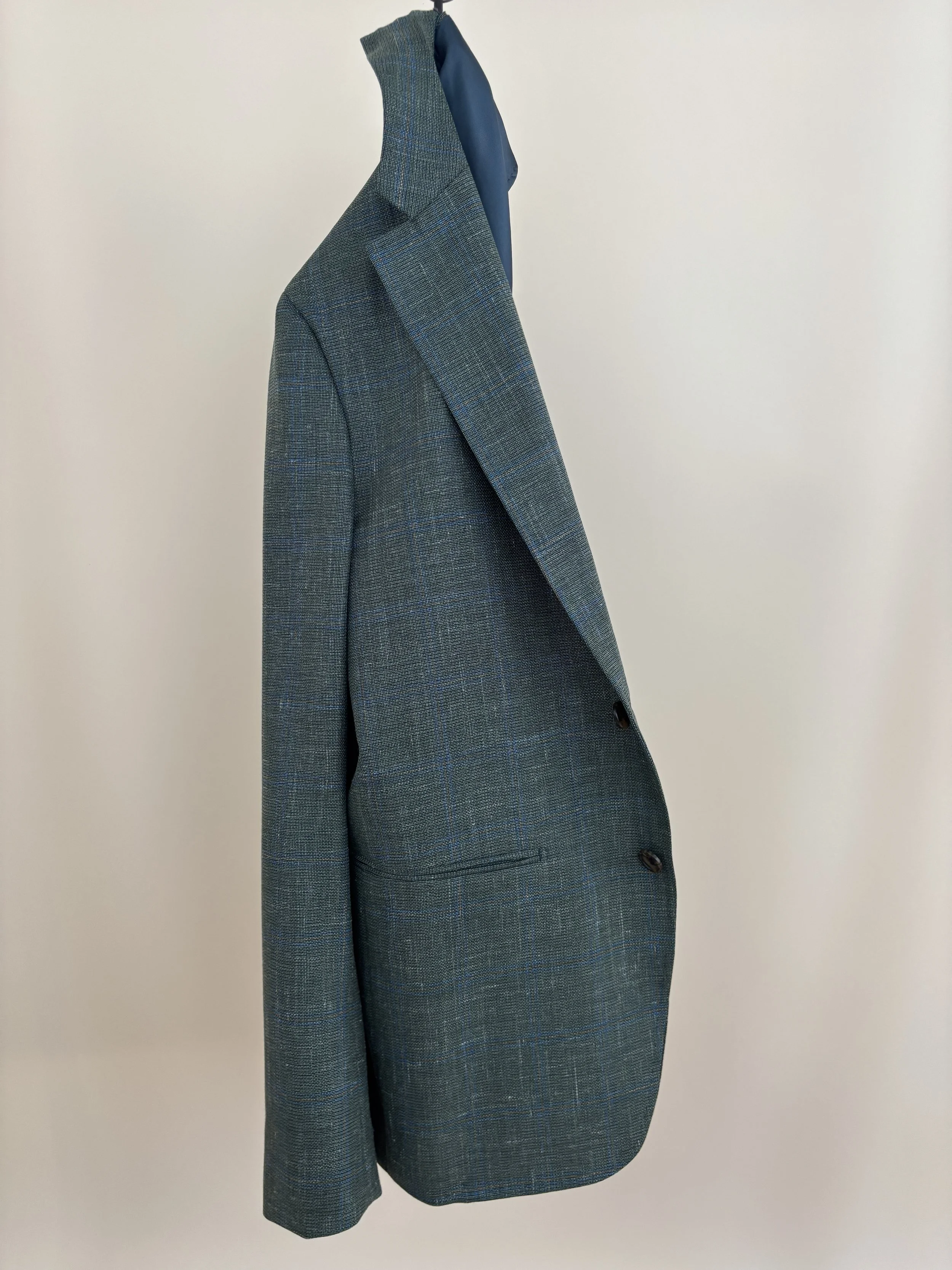 A custom made sage green hopsack windowpane unconstructed blazer against at tan background.
