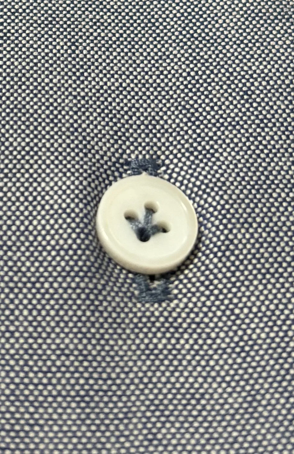 A close up of a mother of pearl shell button with lily stitching on an indigo chambray custom made shirt.