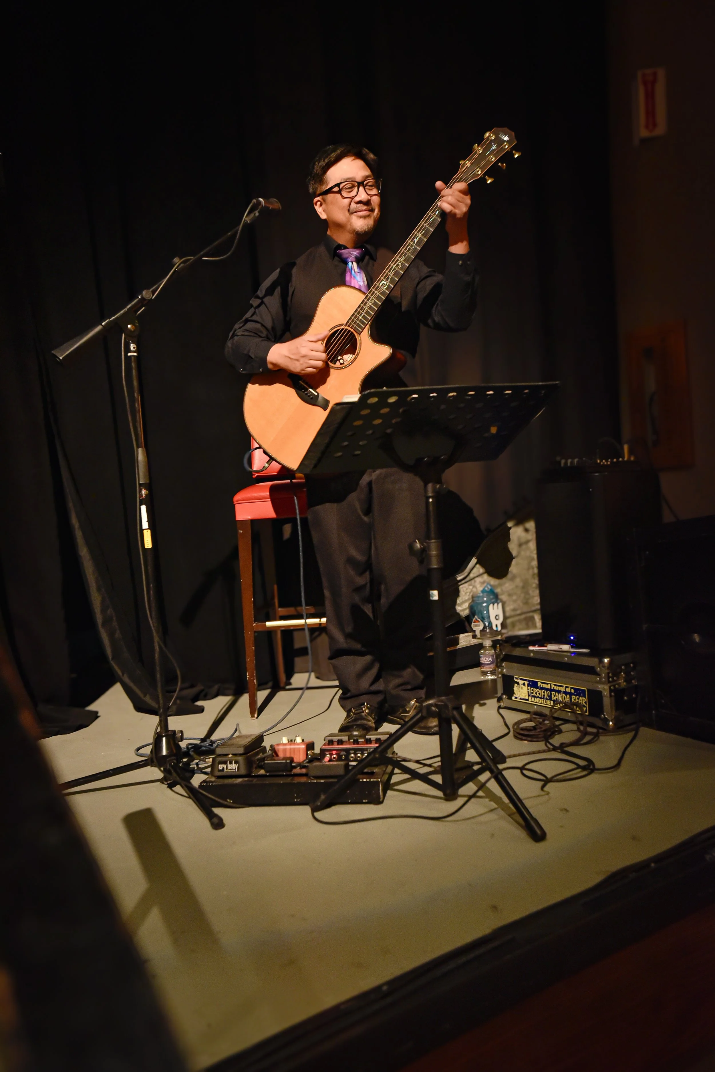 Man playing an acoustic guitar on stage during a concert with music equipment around him.