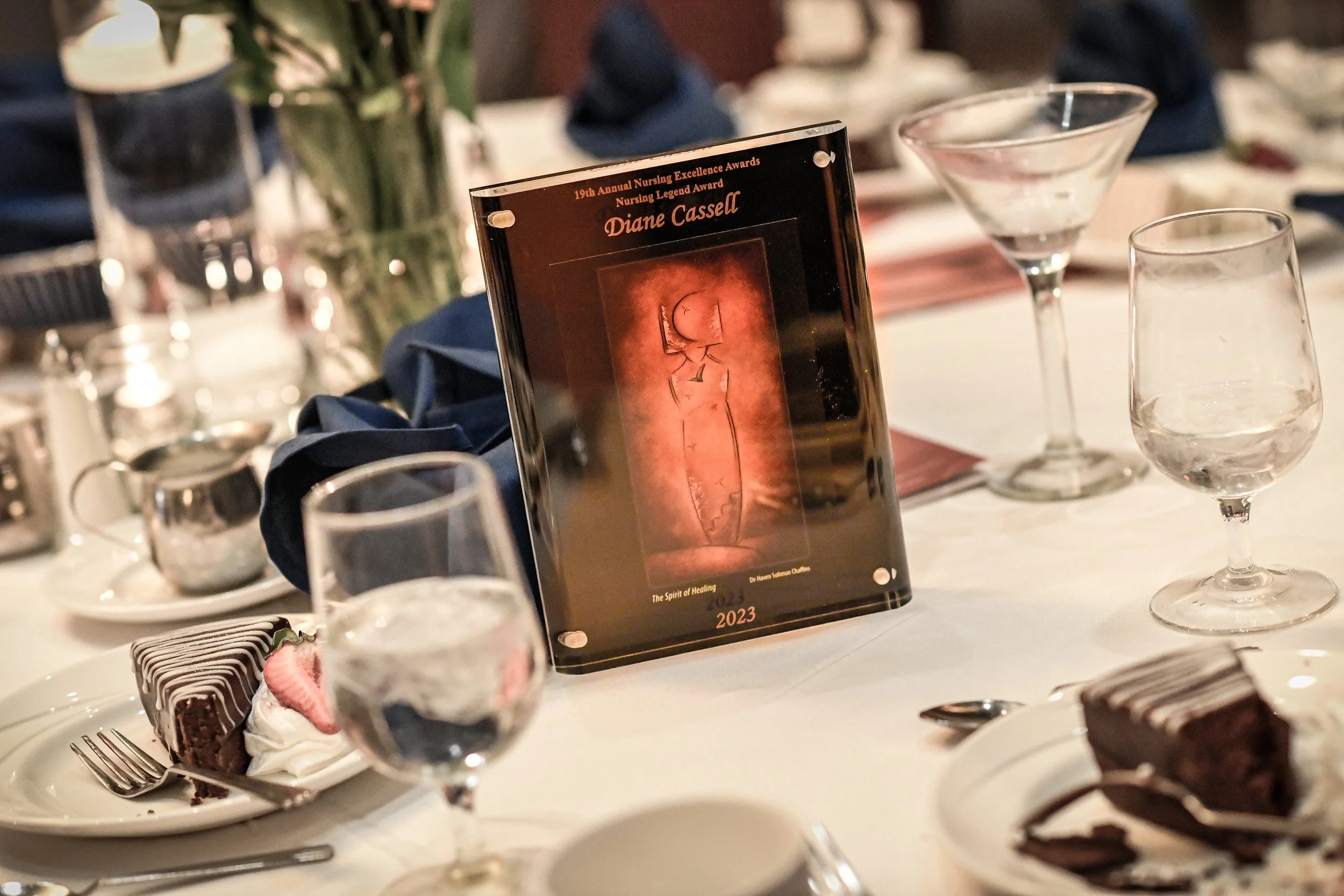 Table with desserts, wine glasses, and a framed award honoring Diane Cassell at a nursing awards event.