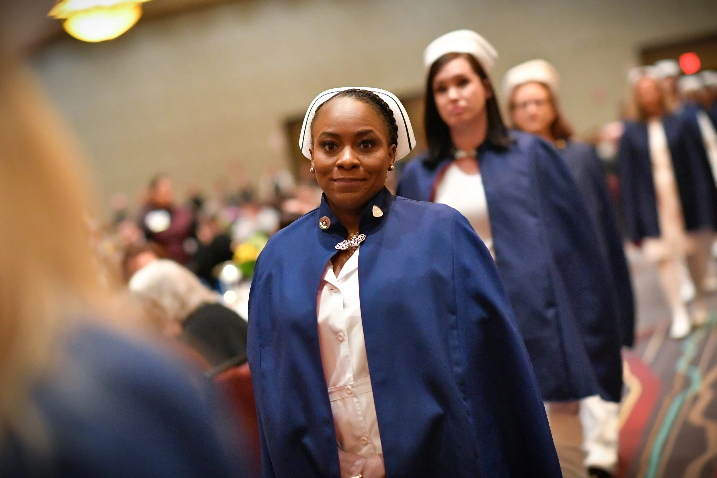 A group of female nurses in blue uniforms and white caps standing in a line at a graduation ceremony.