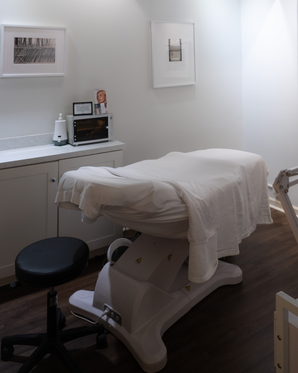 Image of an aestheticians room with a chair for patients. There is a cabinet with medical supplies in the background.