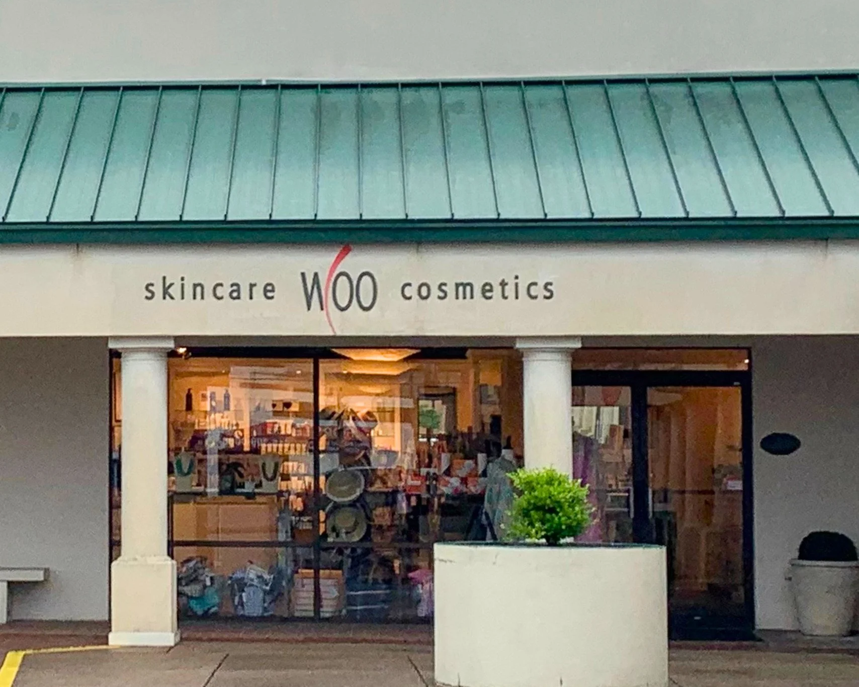 Image of the exterior of woo skincare and cosmetics in Nashville, TN. There is a blue-green awning and two columns in front of the shop window.