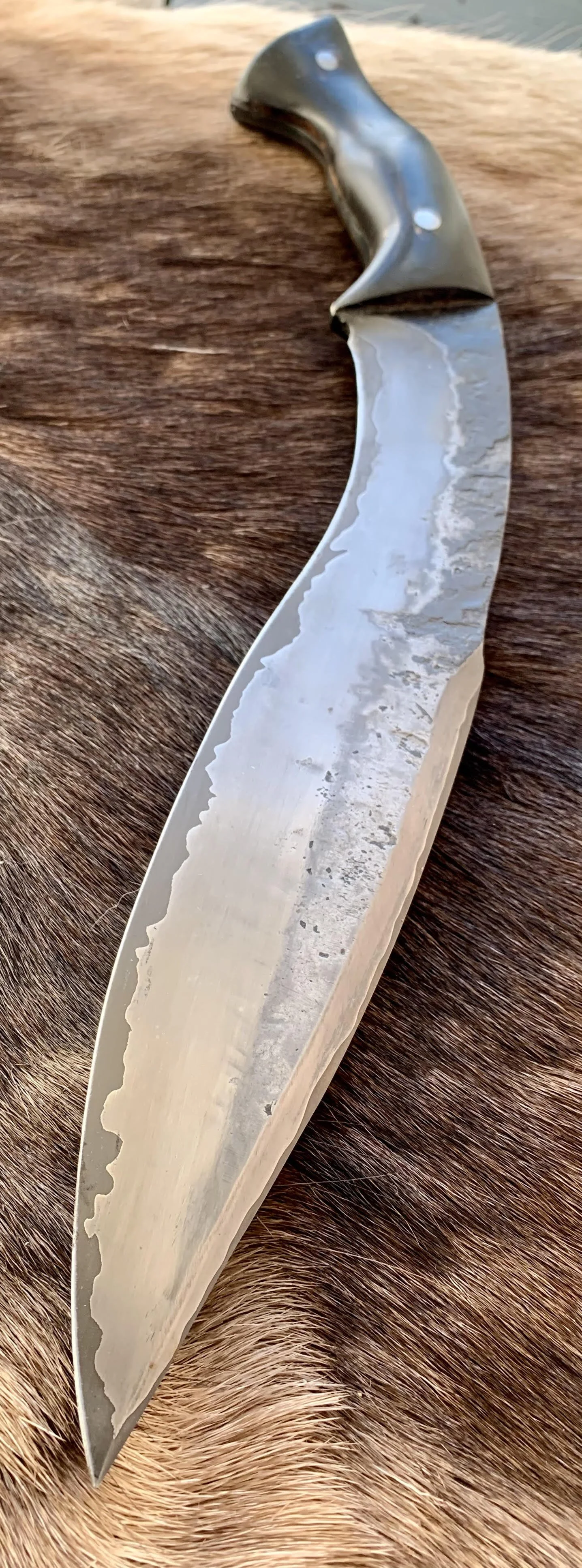 Close-up image of a curved hunting or kitchen knife with a shiny metal blade resting on animal fur.