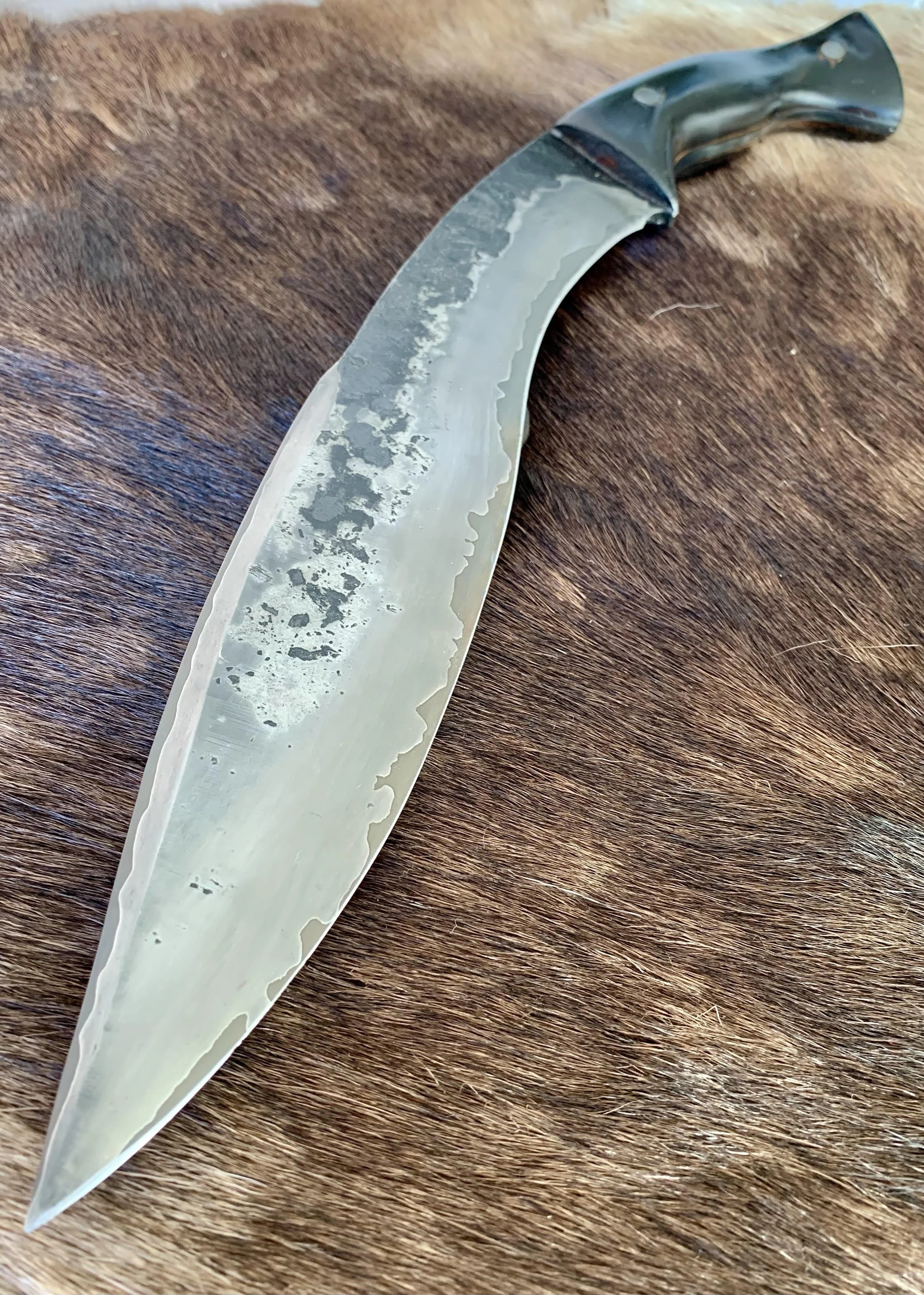 A curved knife with a black handle resting on a brown fur surface.