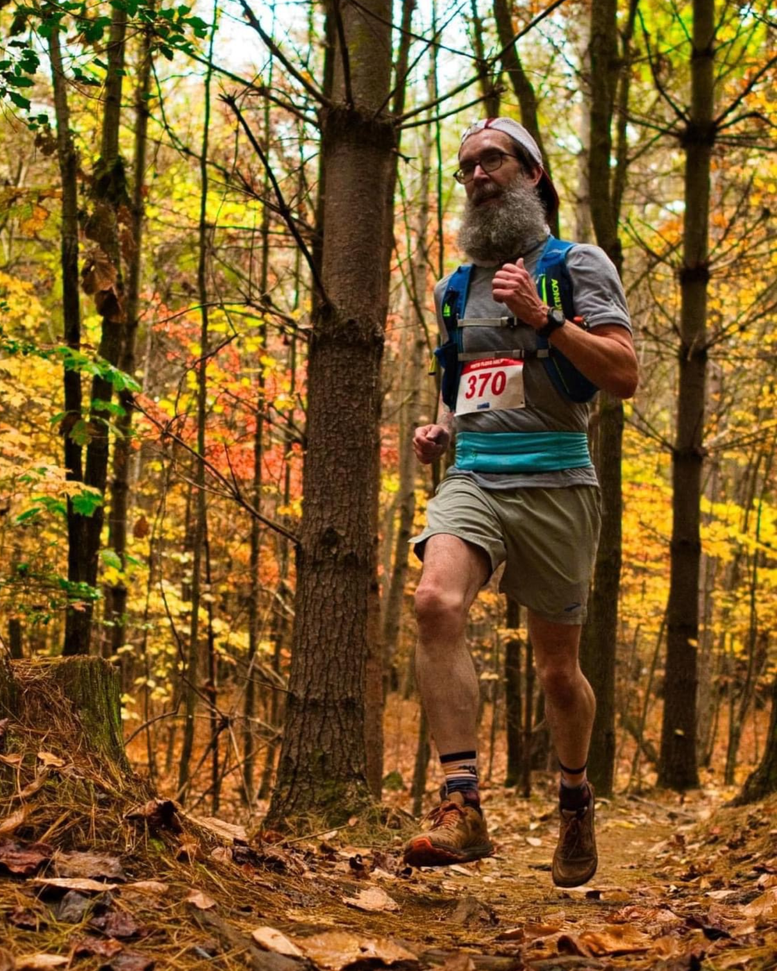 Tim Earley running on a forested trail during a race. He wears a bib with his race number on it.
