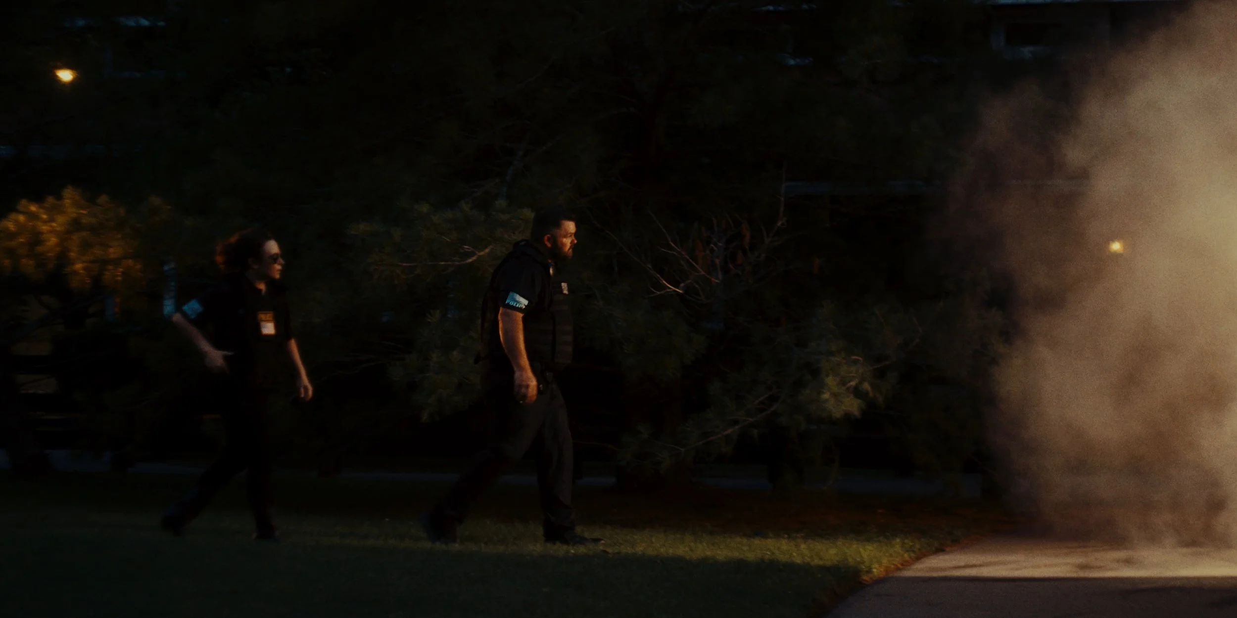 Two police officers walking past a smoldering fire on a sidewalk at night.