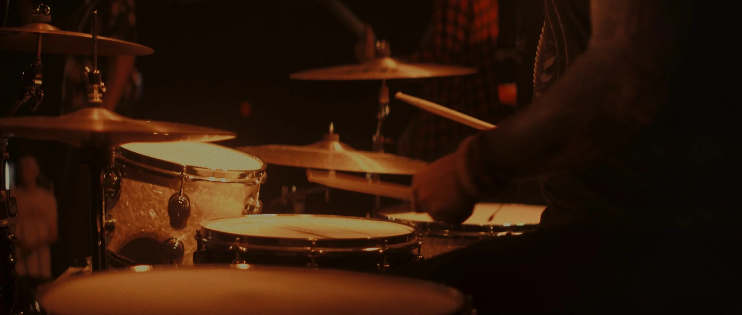 A person playing drums in a dimly lit environment.