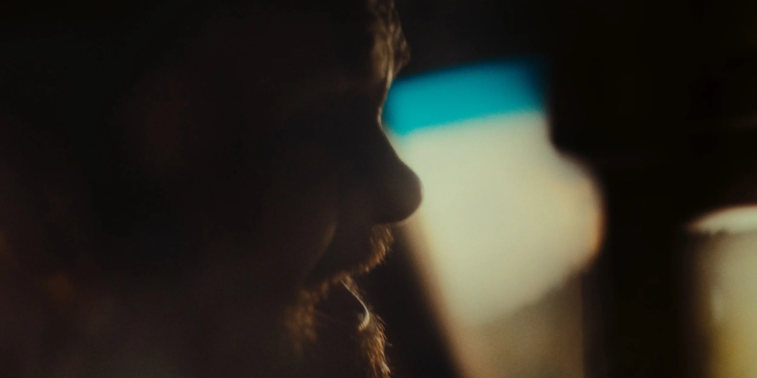 Silhouette of a person with a beard, looking at a phone, with blurred colorful background.