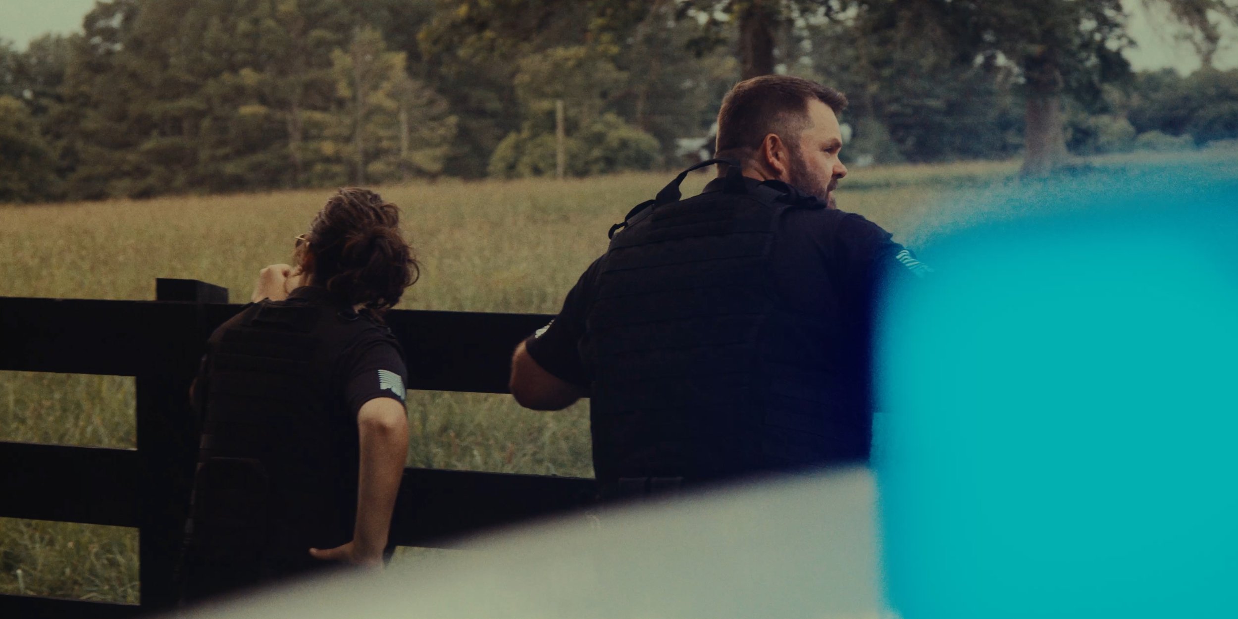 Two police officers, one man and one woman, standing outside during daytime, looking over a rural landscape.