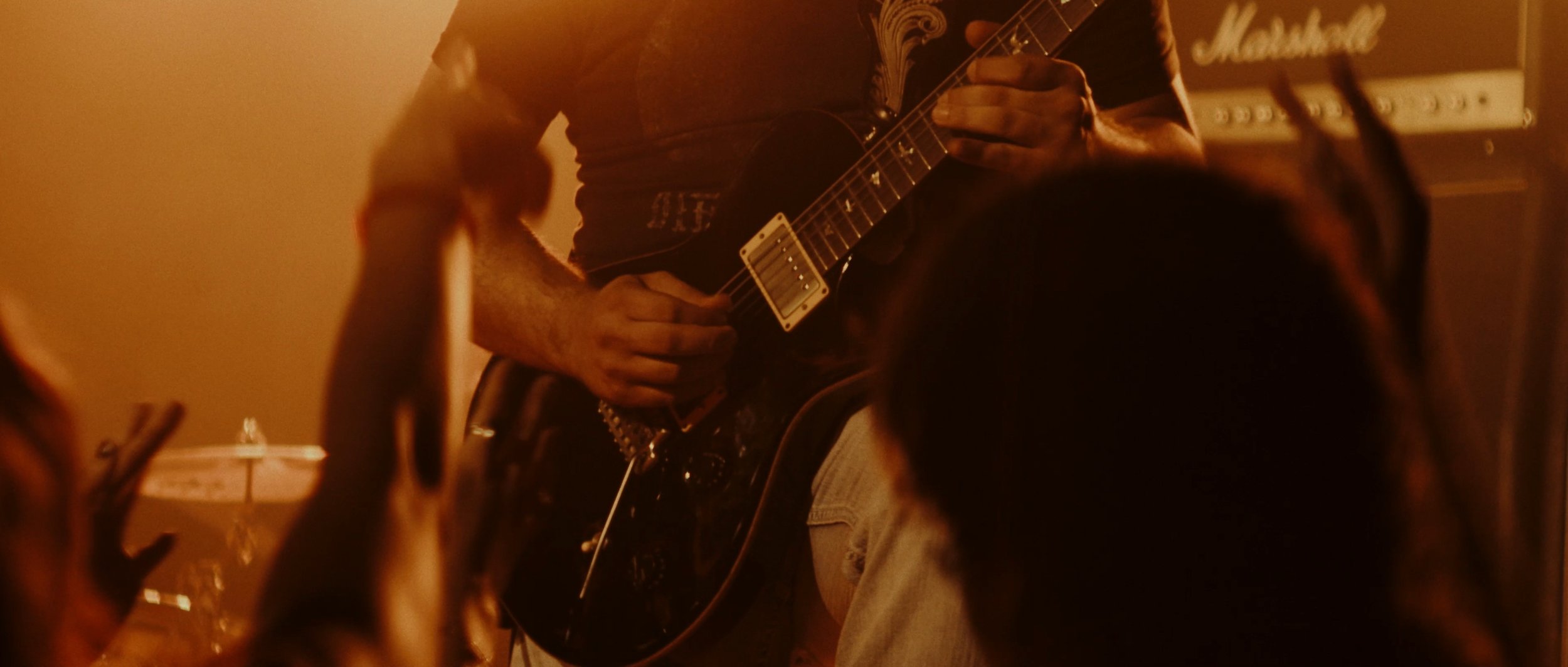 Person playing electric guitar during a live music performance in a dimly lit room.