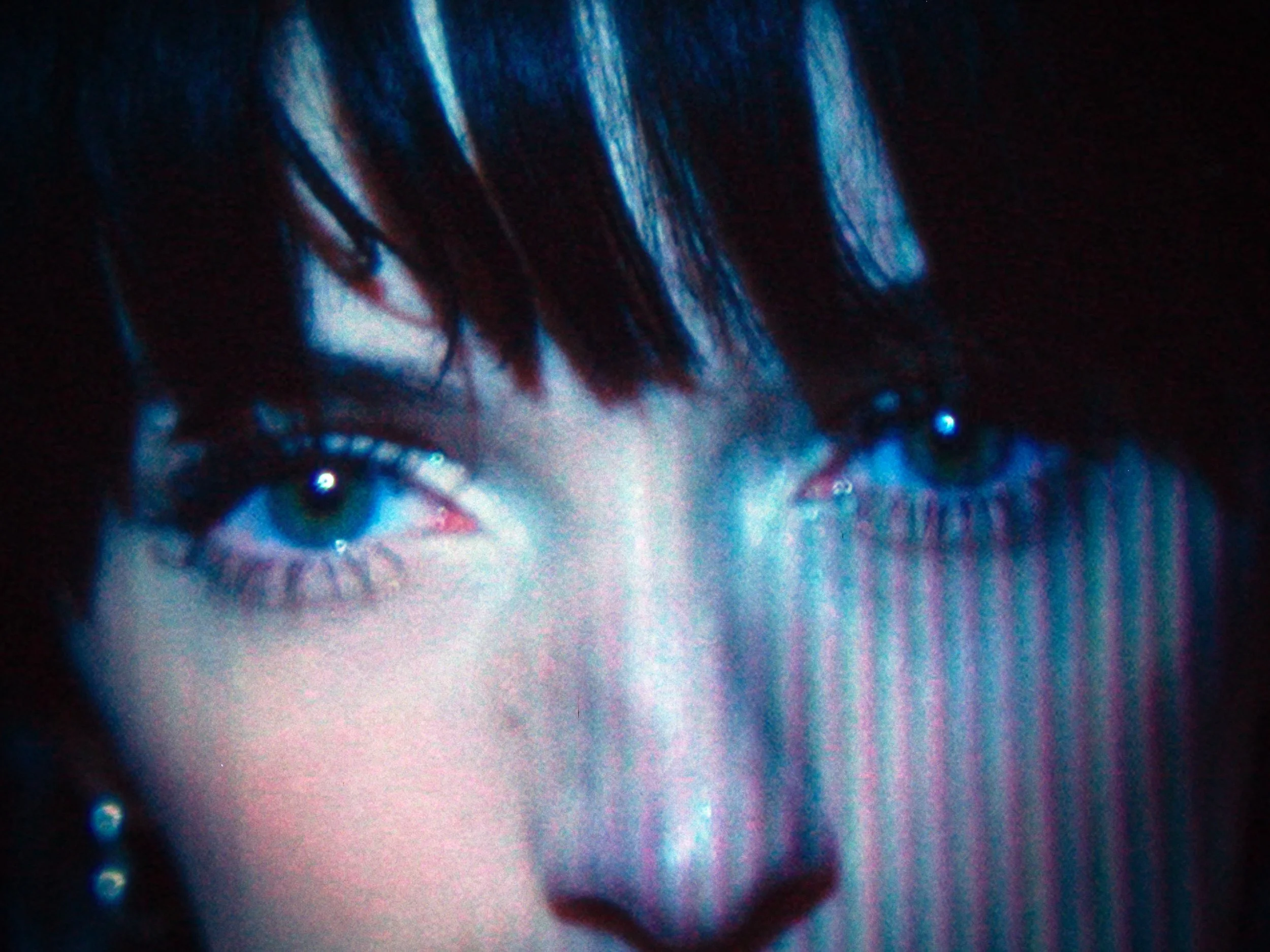 Close-up of a person's face showing blue eyes, dark hair, and a serious expression with a digital glitch effect.