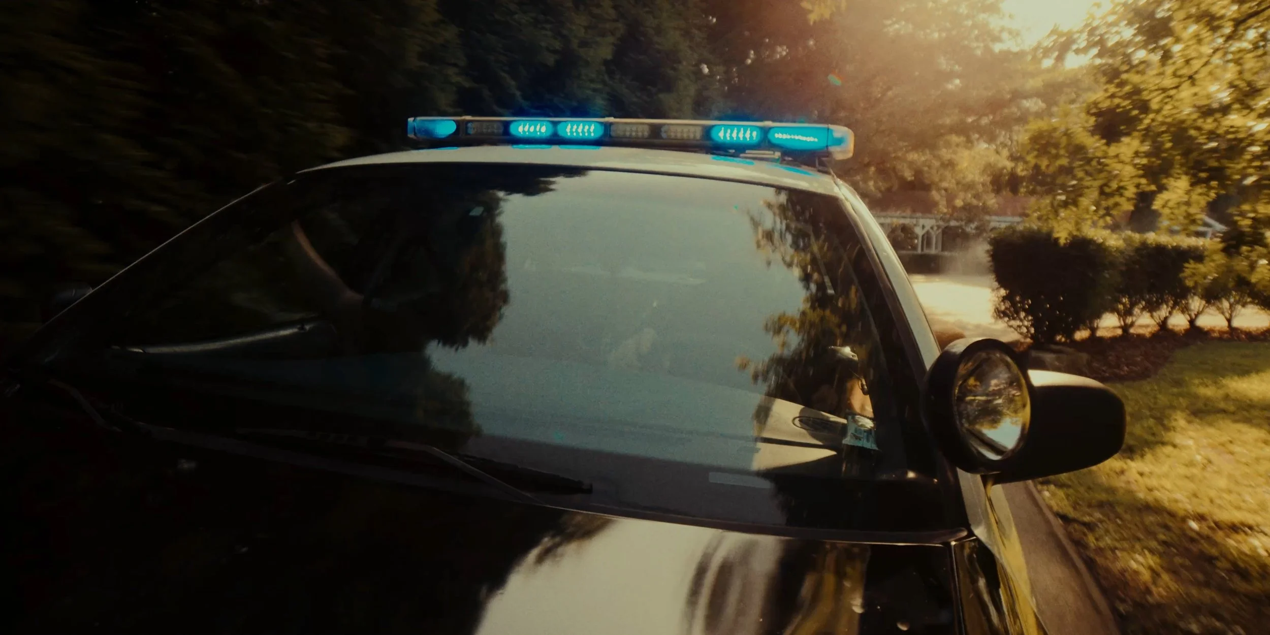Police car with flashing blue lights on a suburban street during sunset.