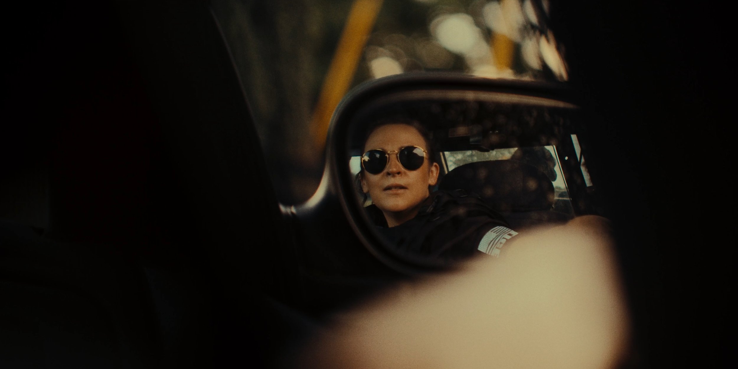 A woman wearing sunglasses is seen through the side mirror of a car.